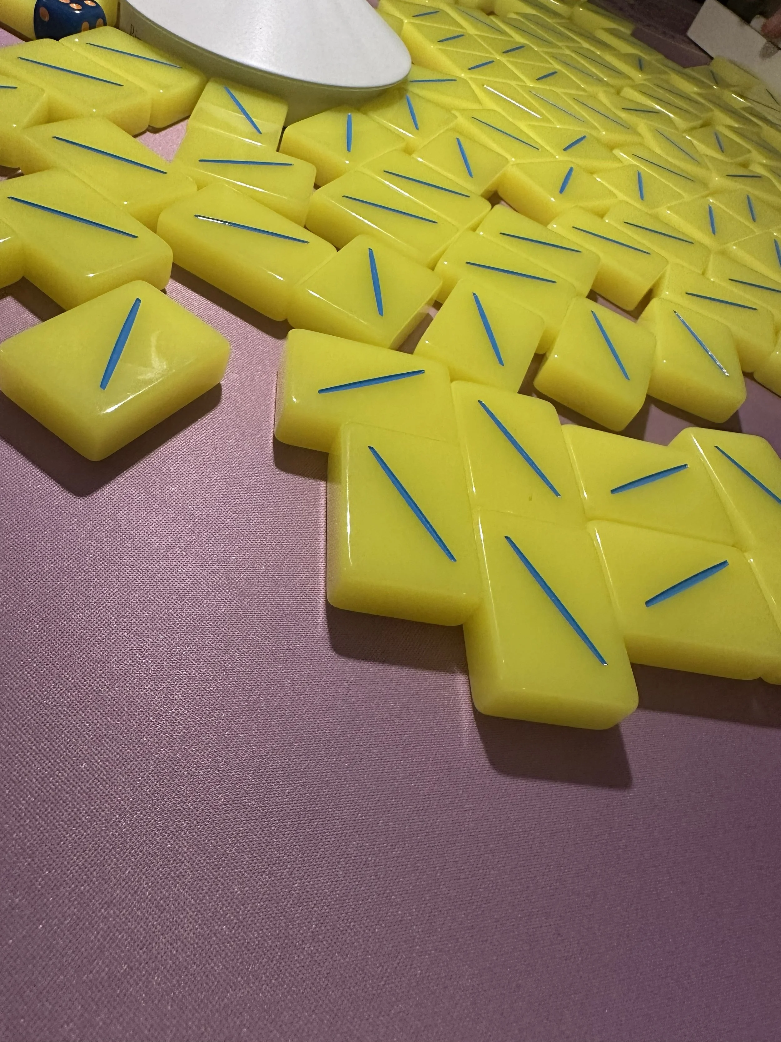 Multiple yellow wax melts with blue sticks, arranged on a pink surface, with a white bowl on top.