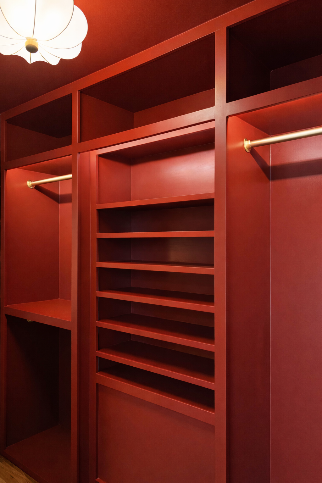Empty custom red closet with open shelves and hanging rods, lit by ceiling light.