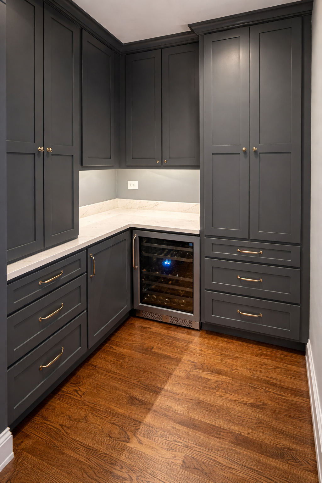 Kitchen corner with dark gray cabinets, white marble countertops, a wine cooler, hardwood floor, and an electrical outlet on the wall.