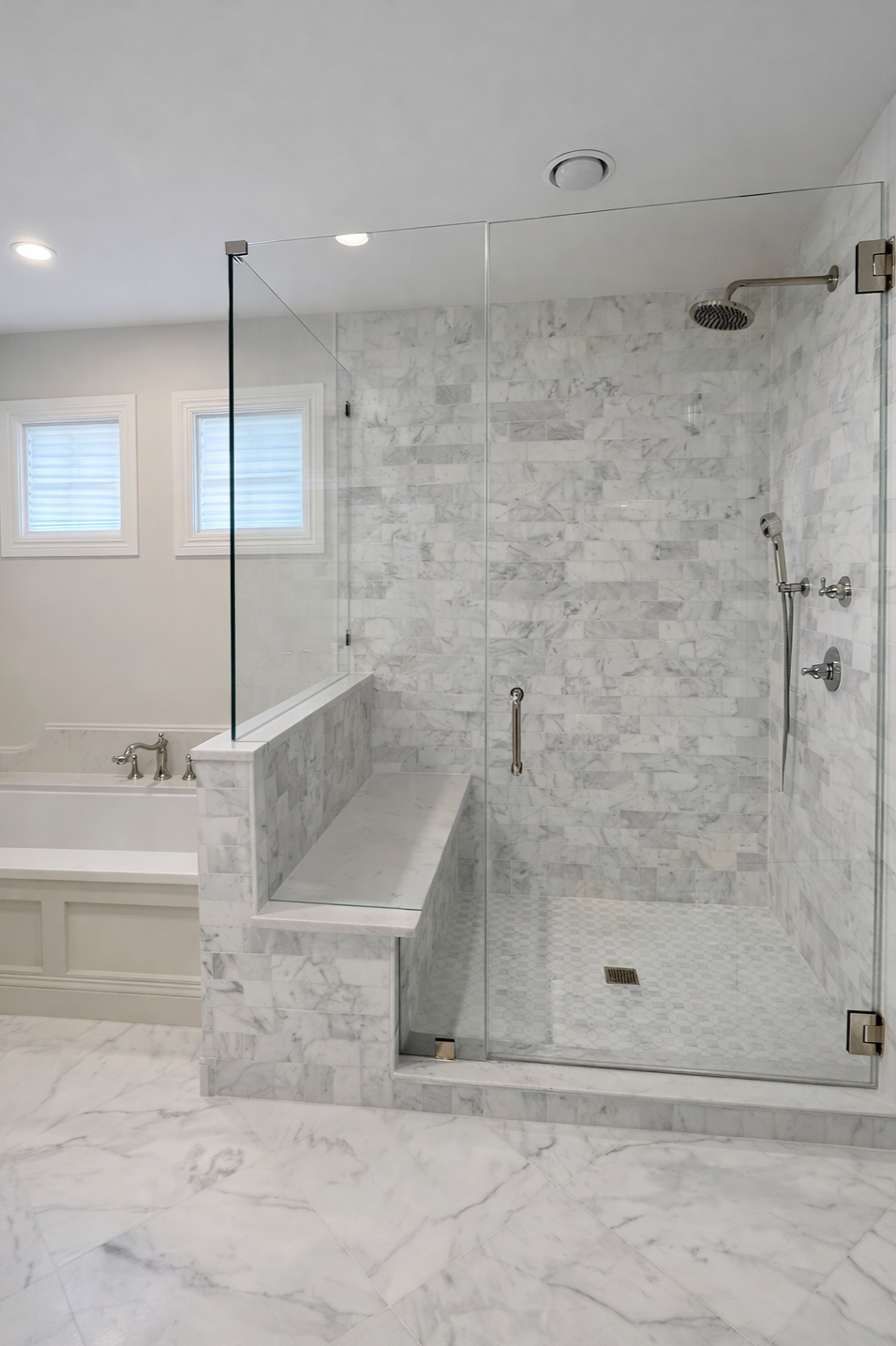 A modern bathroom with a marble shower and bathtub, two small windows, and white marble flooring.