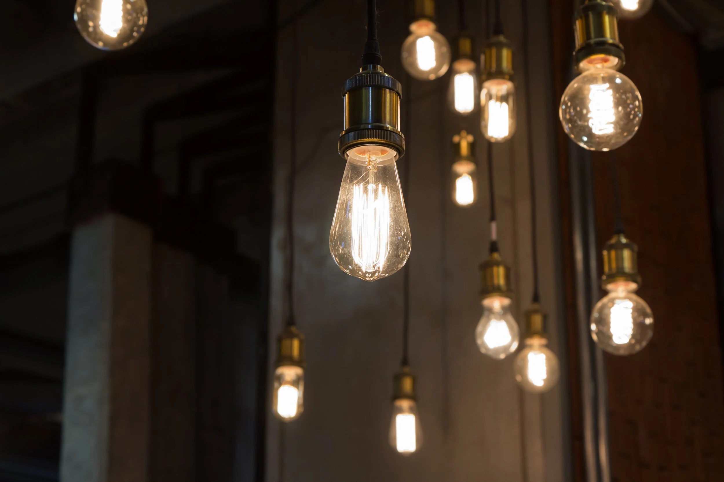 Group of hanging Edison-style light bulbs with warm glow in a dark interior space.