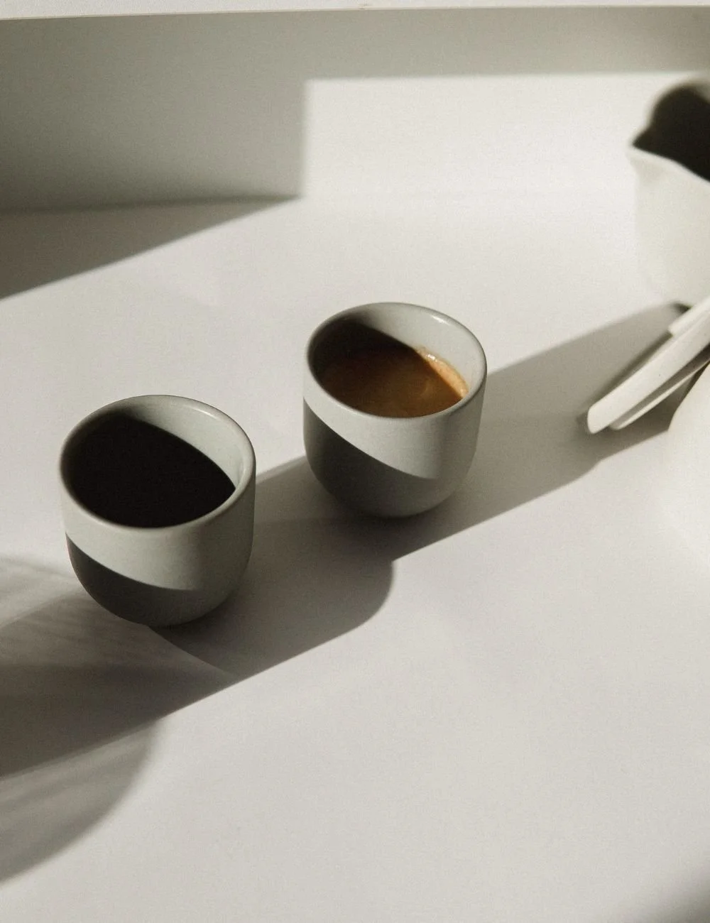 Two cups of coffee on a white surface, casting shadows with a pair of white scissors to the right.