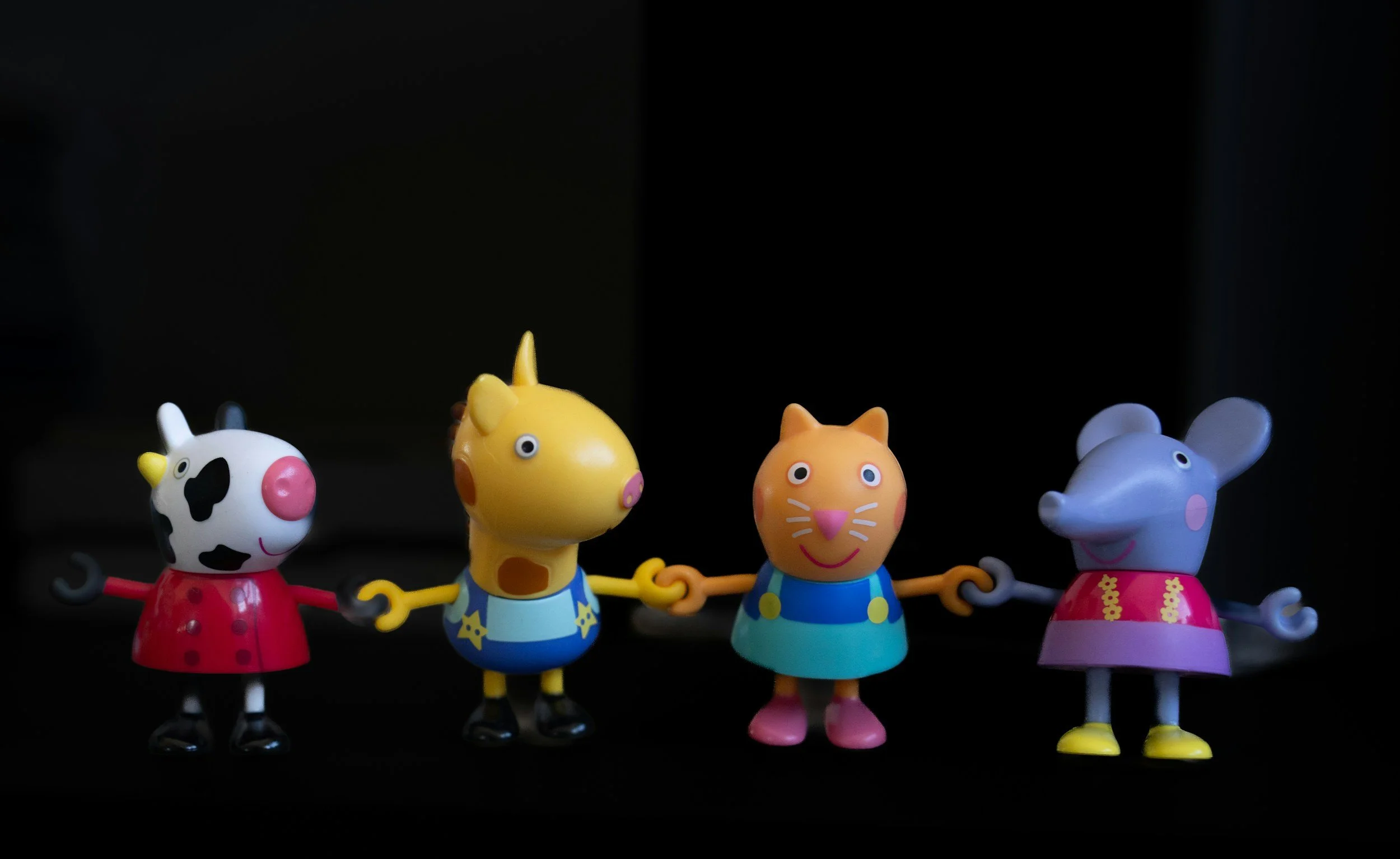 A row of four colorful animal-themed figurines holding hands with a dark background.