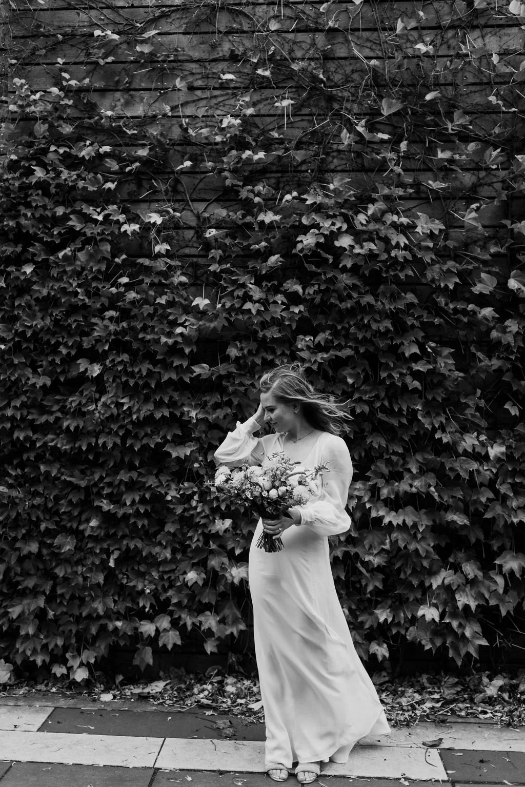 Bride outside by an ivy wall adjusting her hair
