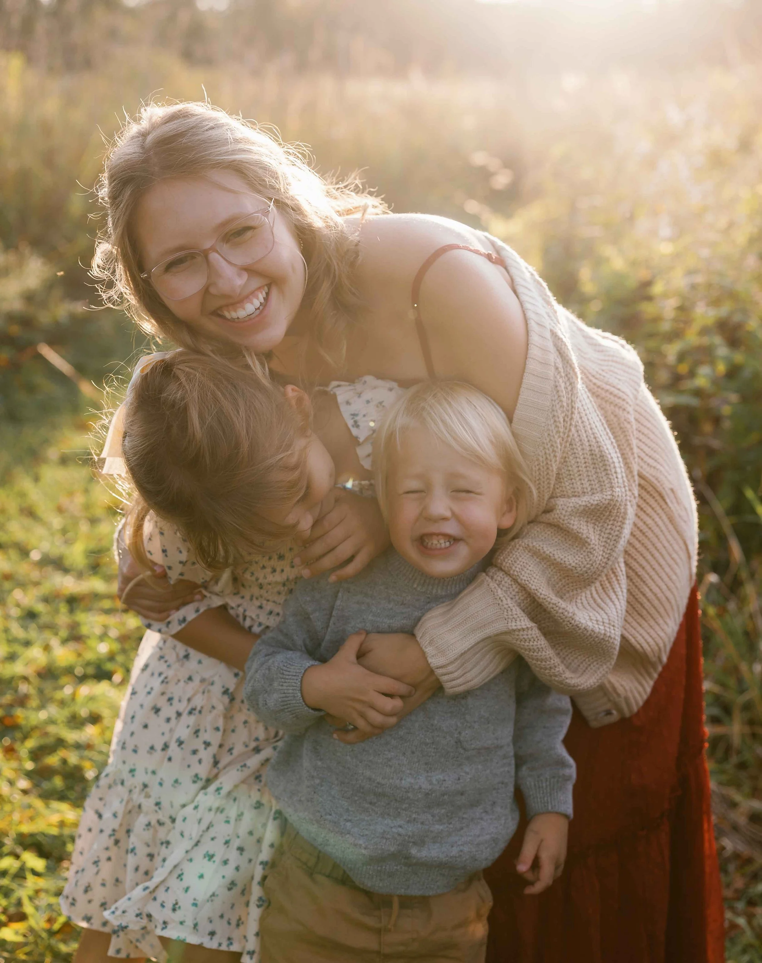 Outside at the Morton Arboretum a mom is hugging her two young kids