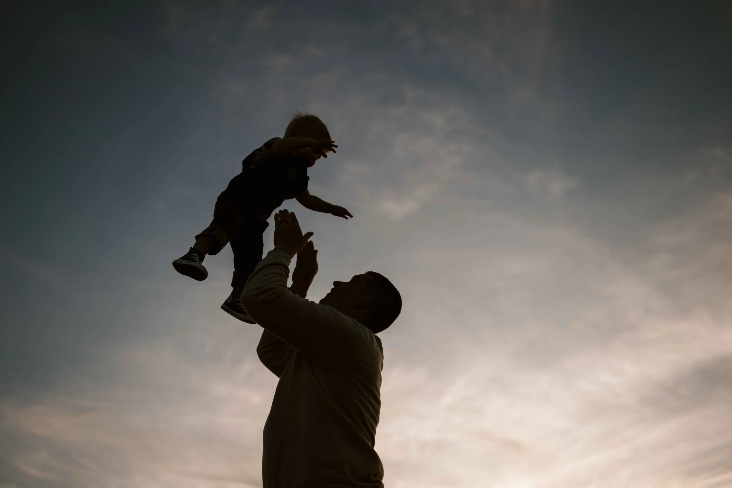 Sunset silhouette of dad throwing son in the air at Blackwell Forest Preserve in Wheaton IL