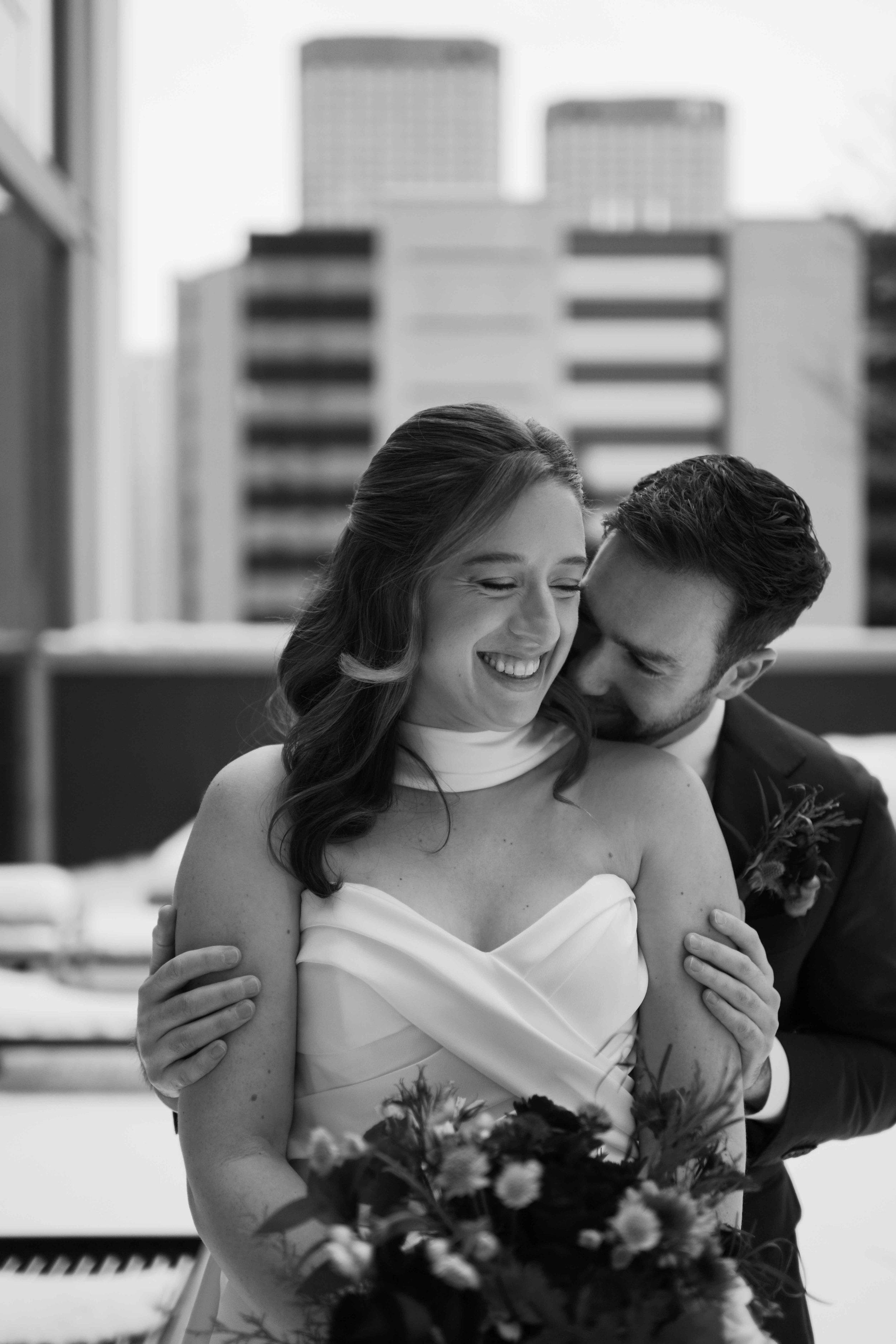 black and white photo of bride and groom with groom hugging the bride from behind on rooftop of chicago hotel