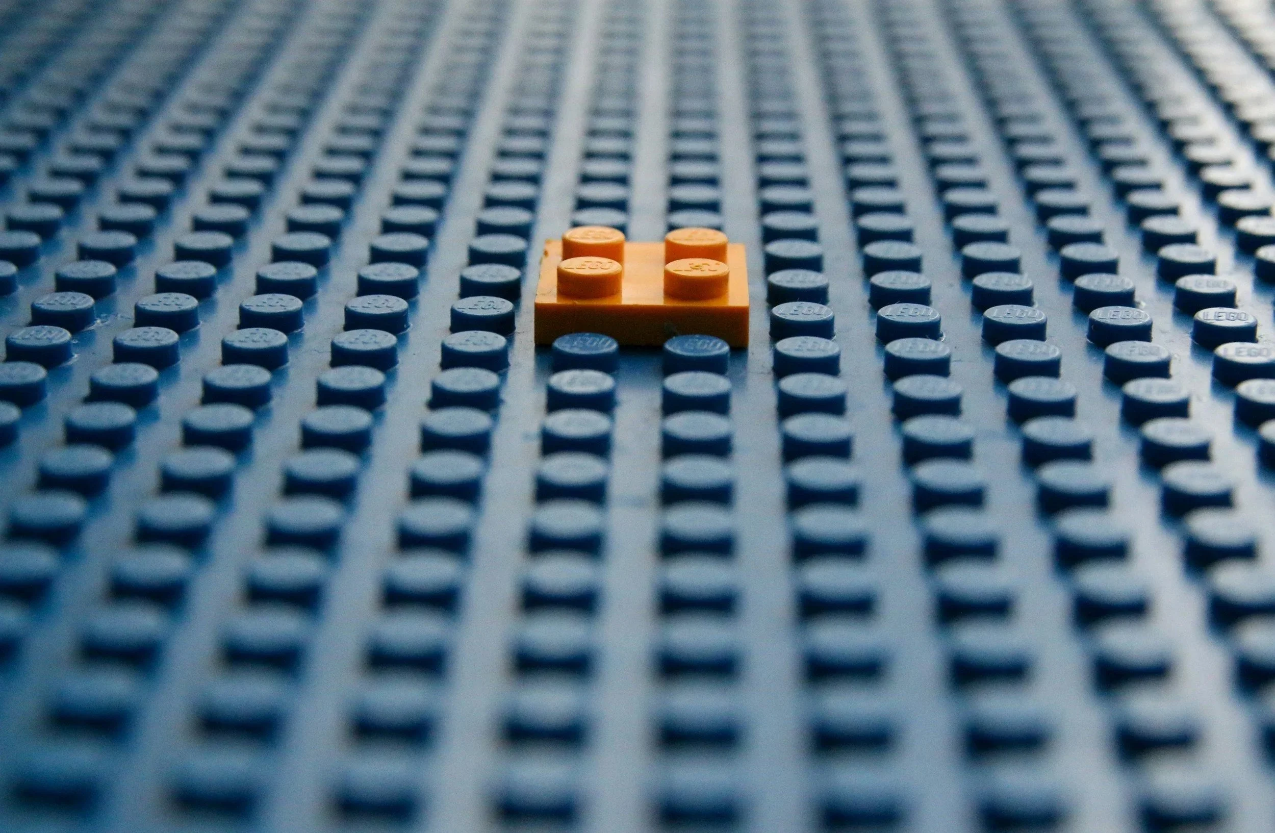 Close-up of a large blue LEGO baseplate with a single orange LEGO brick placed in the center.