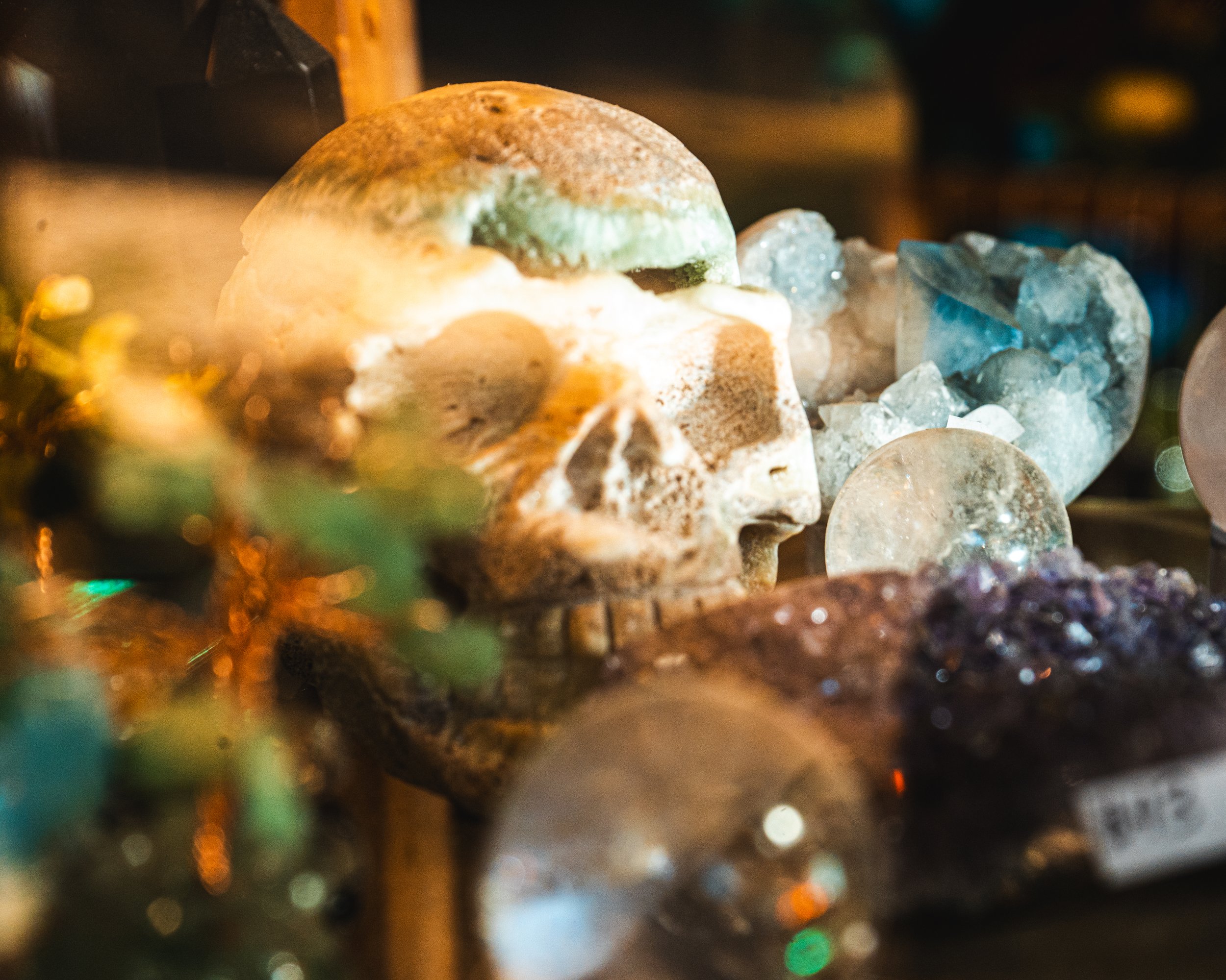 A human skull sculpture surrounded by various crystals and minerals.