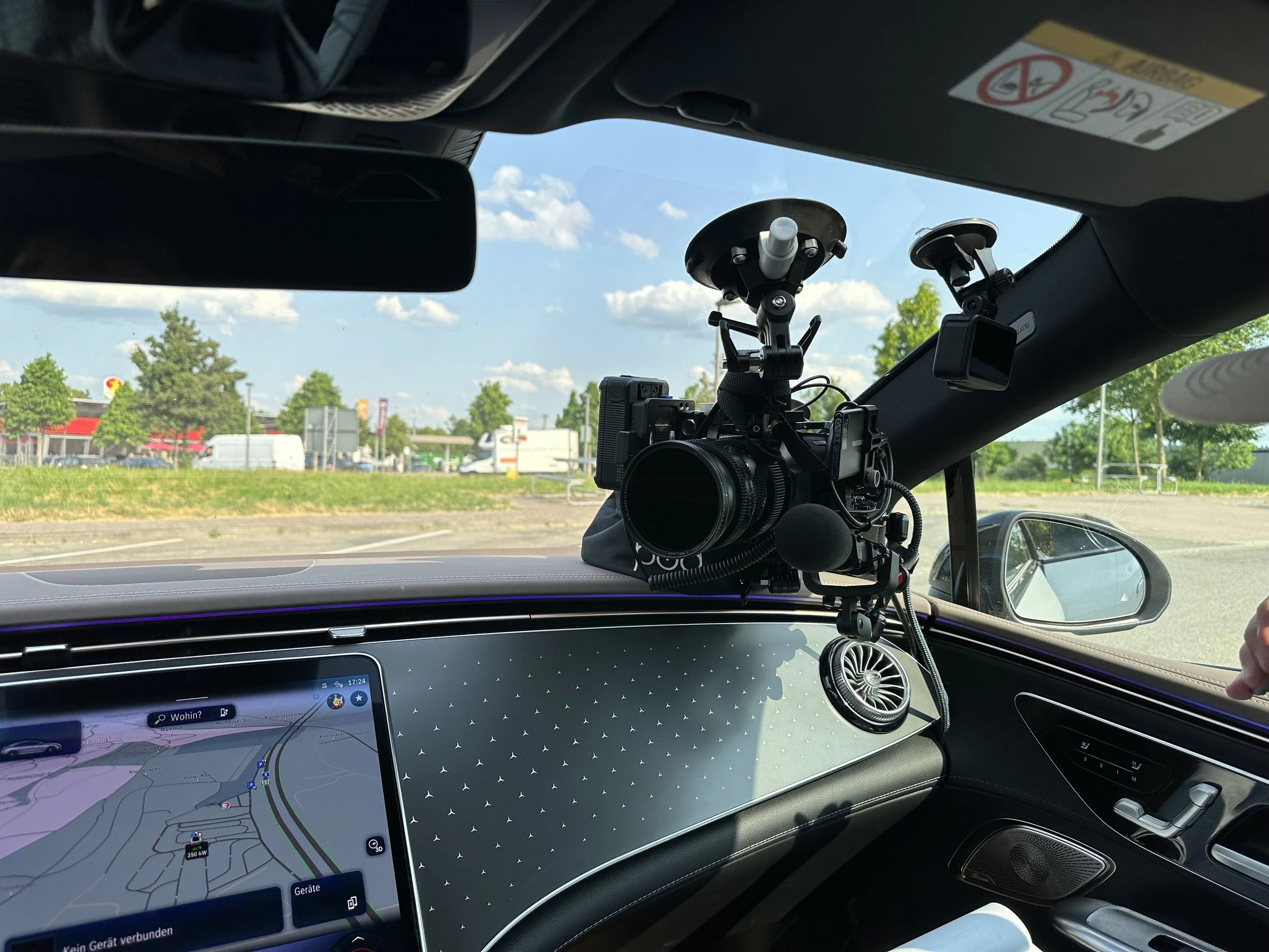 Innenansicht eines Autos mit einer Kamera auf einem Halter an der Windschutzscheibe, während die Straße und bunte Geschäfte draußen sichtbar sind.