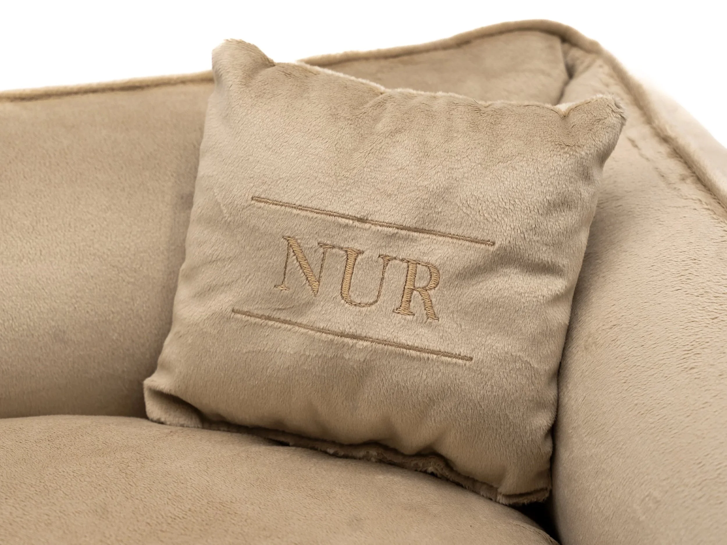 Un cuscino di colore beige con una copertina di stoffa bordata, su cui è ricamata la parola "NUR".