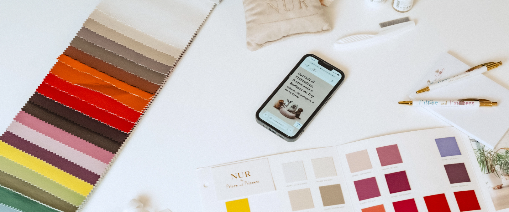 Tavolo con campioni di tessuto, catalogo di colori, penne e uno smartphone con pagina web aperta