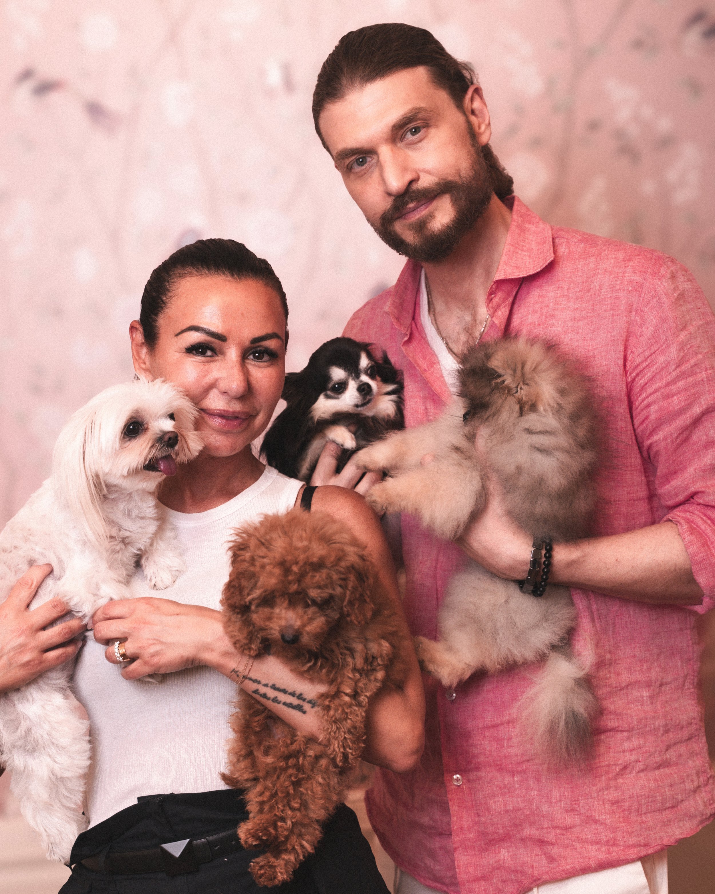 Una donna e un uomo sorridenti tengono dei cani di diverse razze e dimensioni in braccio. La donna indossa una maglietta bianca, l'uomo una camicia rossa. Lo sfondo è sfocato.