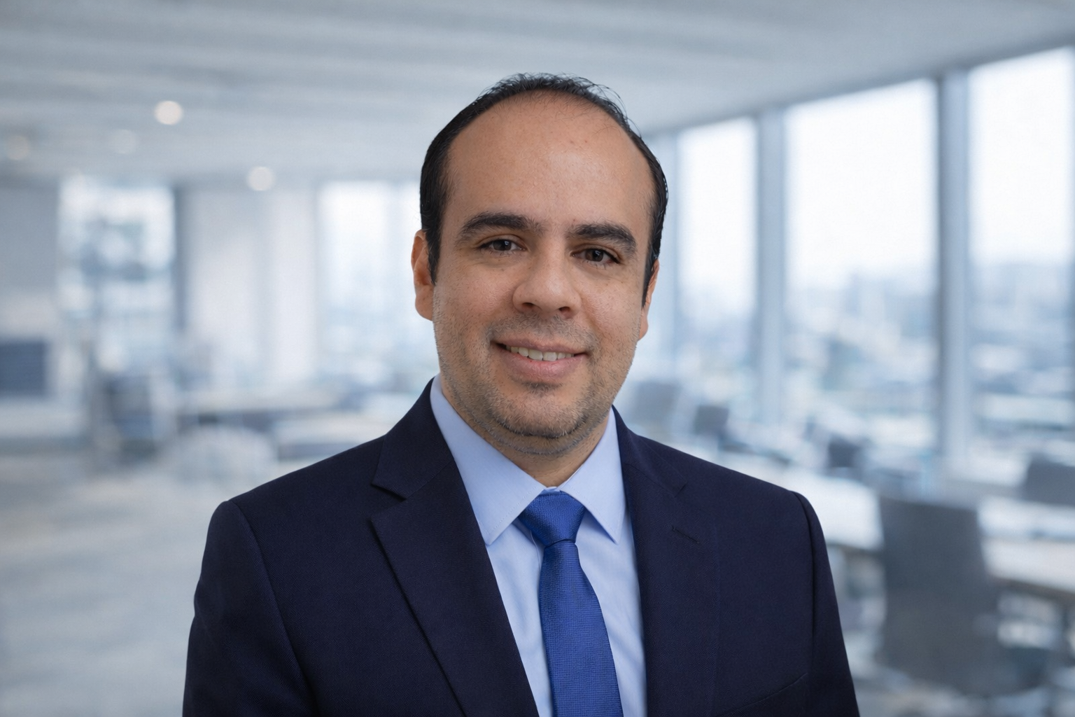 Retrato de un hombre con traje y corbata en una oficina moderna con ventanas grandes.