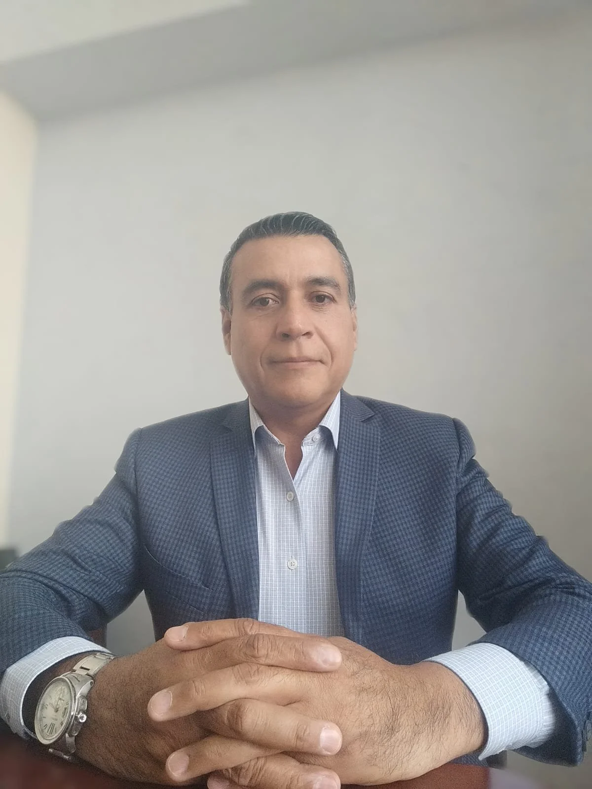 Retrato de un hombre sentado en una mesa, con vestimenta formal, mostrando una expresión neutral.