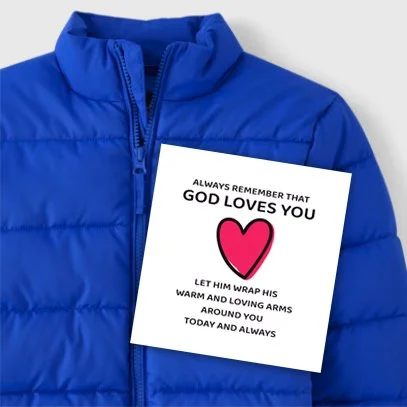 Blue puffer jacket with a white card featuring a pink heart and the message: Always remember that God loves you, let Him wrap His warm and loving arms around you today and always.