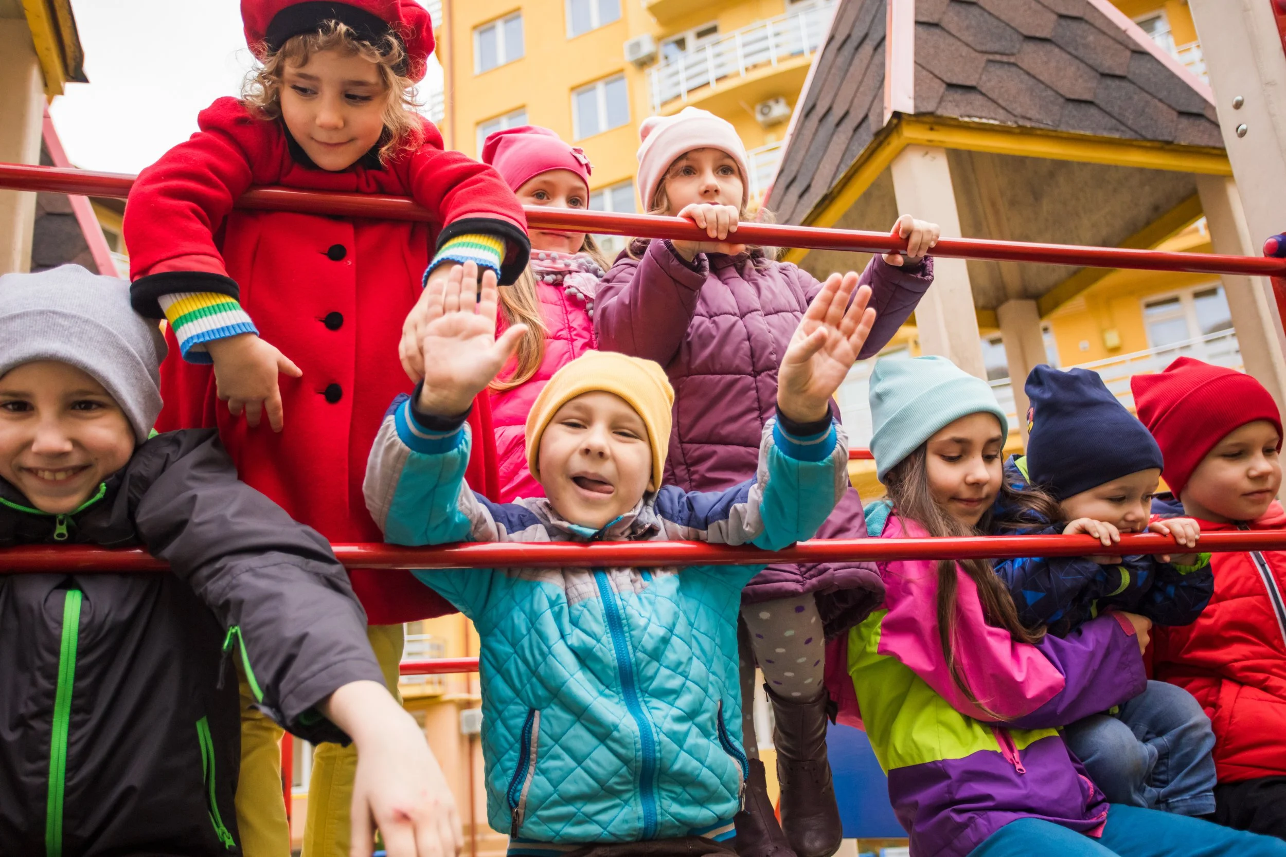 Group of young children wearing jackets and hats playing on a playground.