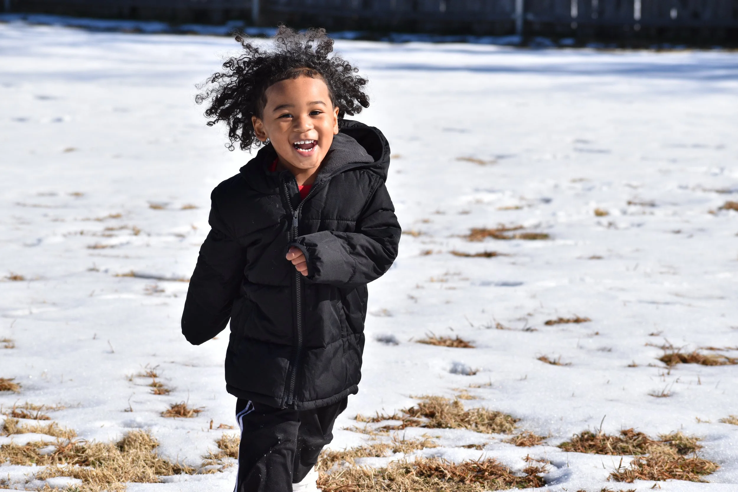 Young girl running and smiling on snow-covered ground in winter.
