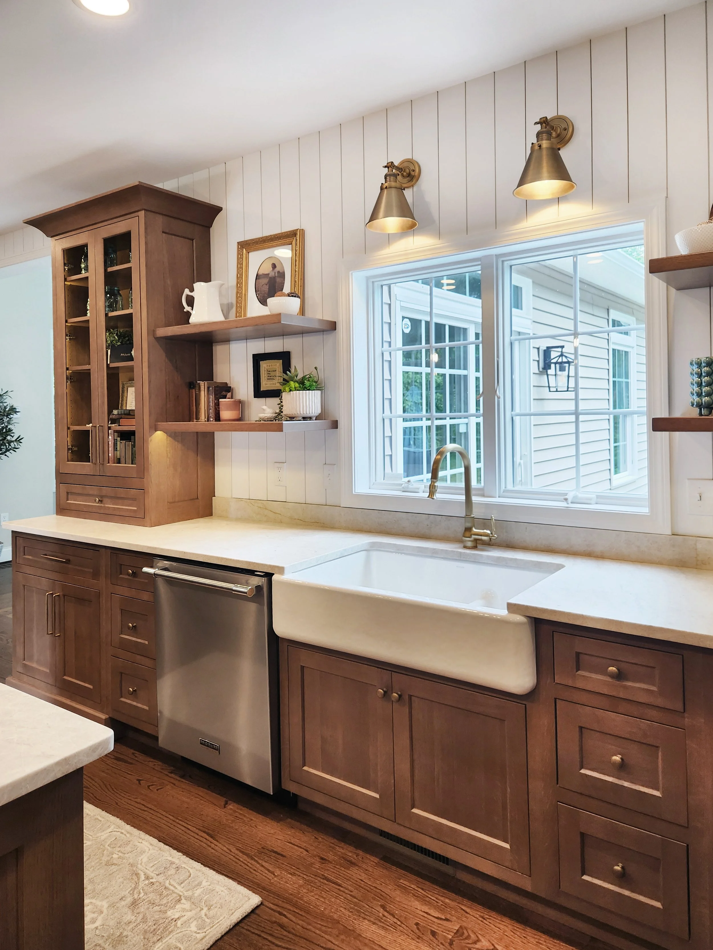 Kitchen with wooden cabinets, a farmhouse sink, a window above the sink, and open shelves with decorative items.
