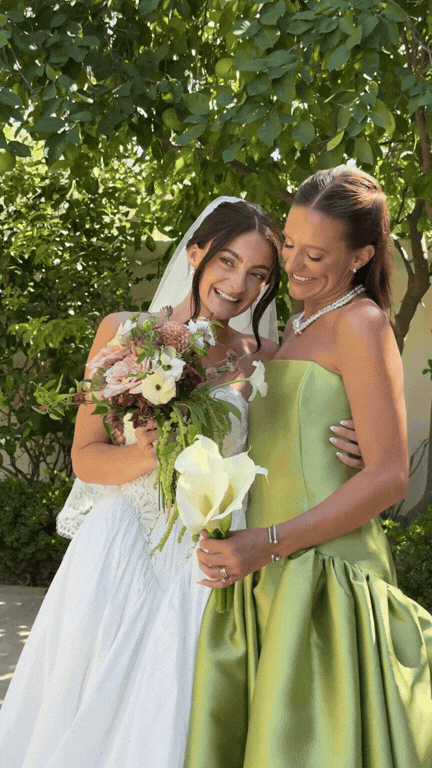 A bride in a white gown embracing her bridesmaid in a satin chartreuse gown.