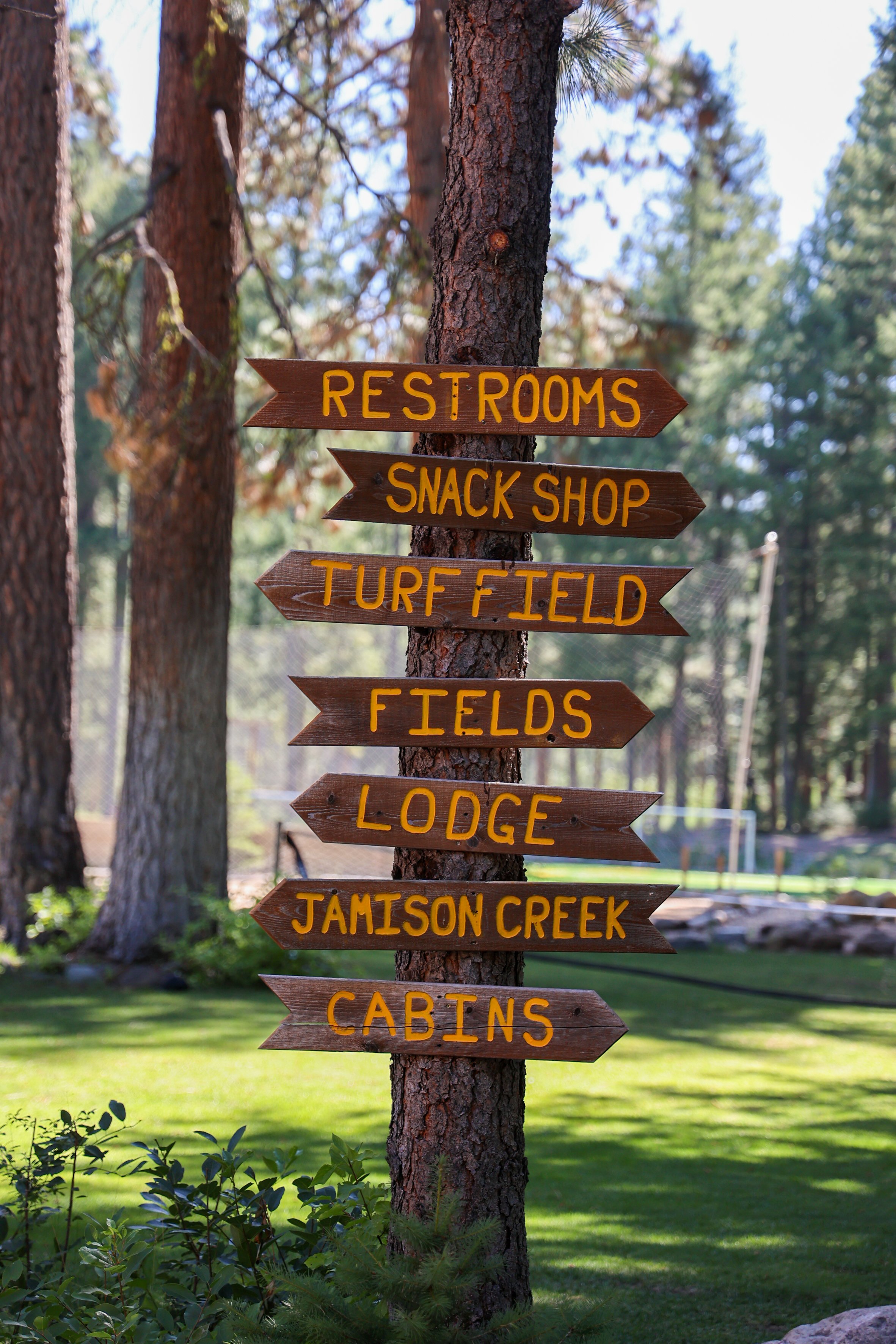 Wooden signpost pointing to camp areas including fields, cabins, and dining hall at Two Rivers