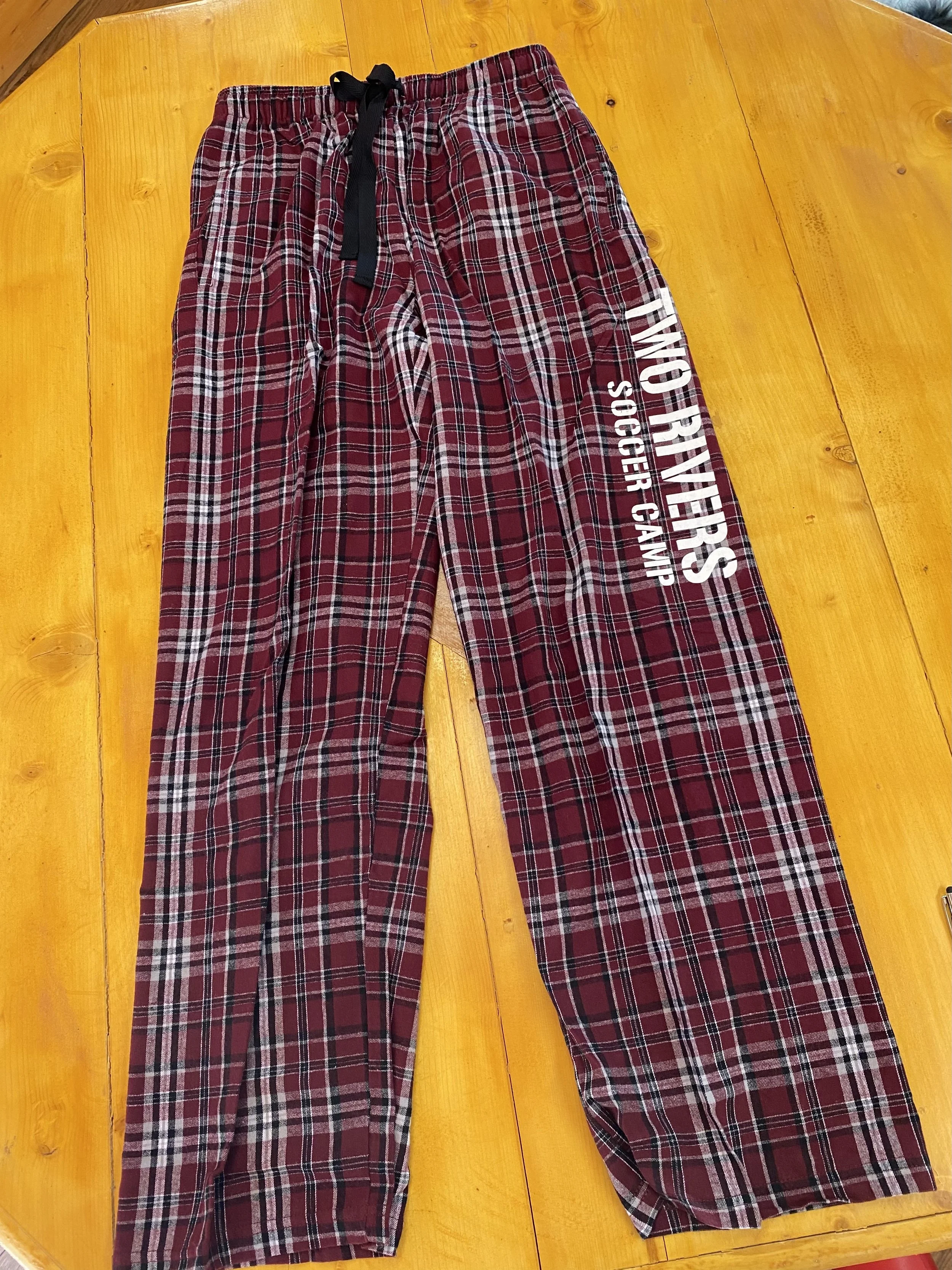 Red plaid pajama pants with white text that reads "Oregon Ducks Soccer Camp" on the left leg, laid flat on a wooden surface.