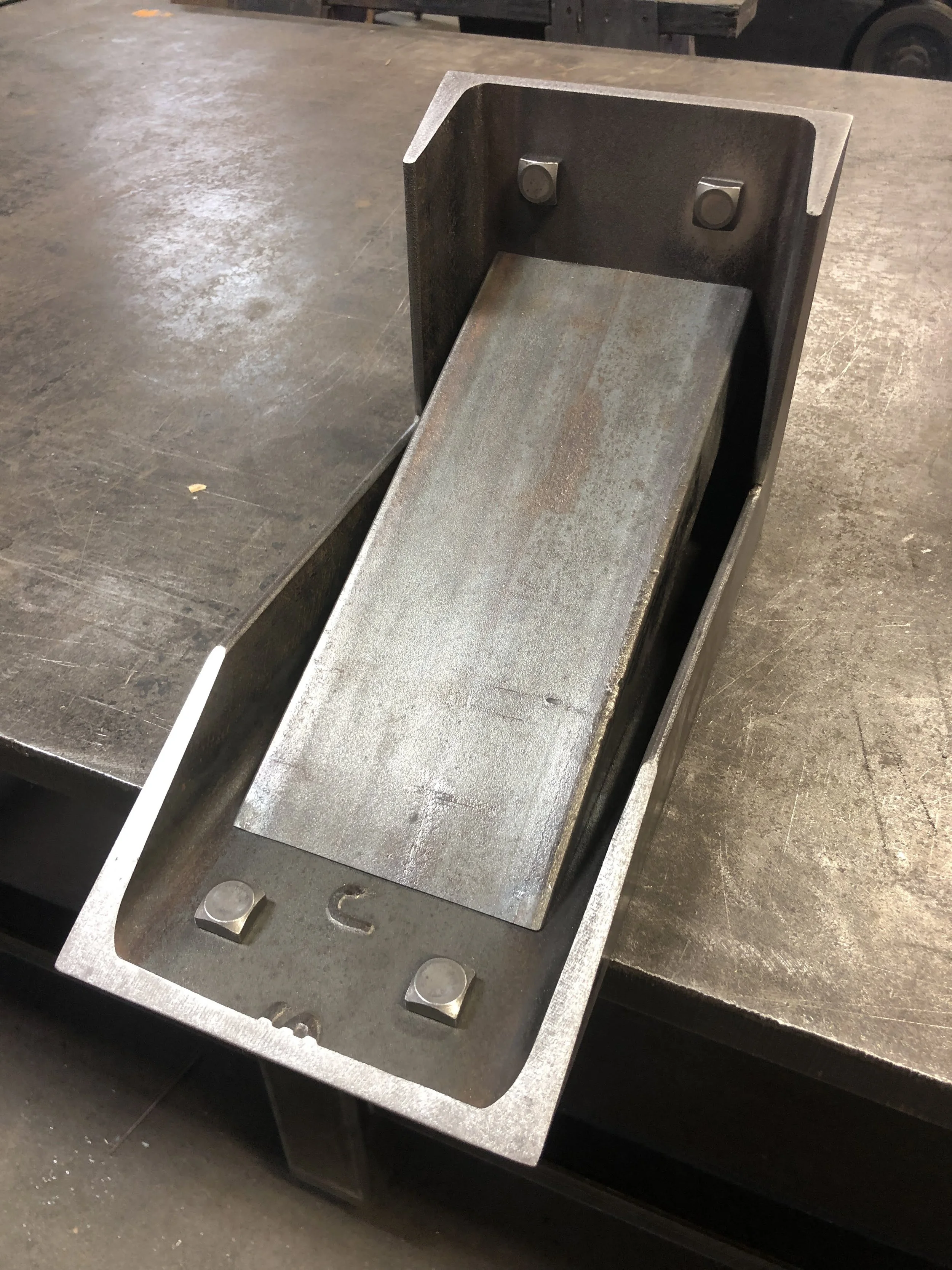 Metal metal fabrication jig or part with four screws on a workbench.