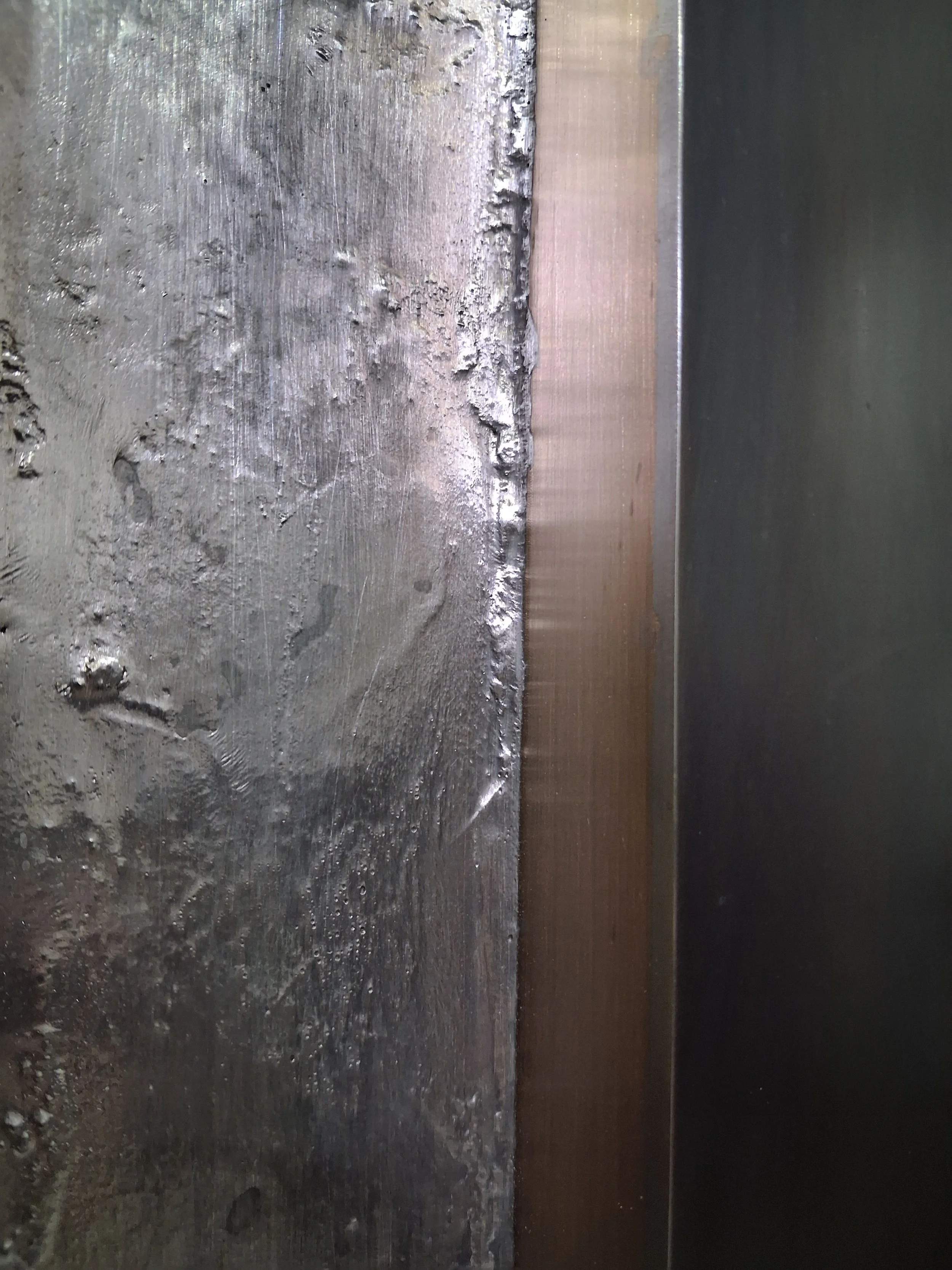 Close-up of a metal surface with rough, uneven texture next to a smooth, polished edge.