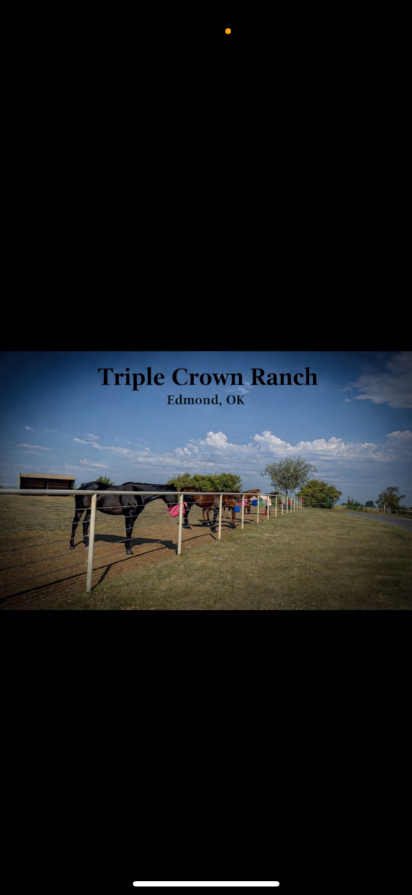 Sign reading 'Triple Crown Ranch, Edmond, OK' with horses grazing behind a fence on a sunny day with a blue sky and scattered clouds.