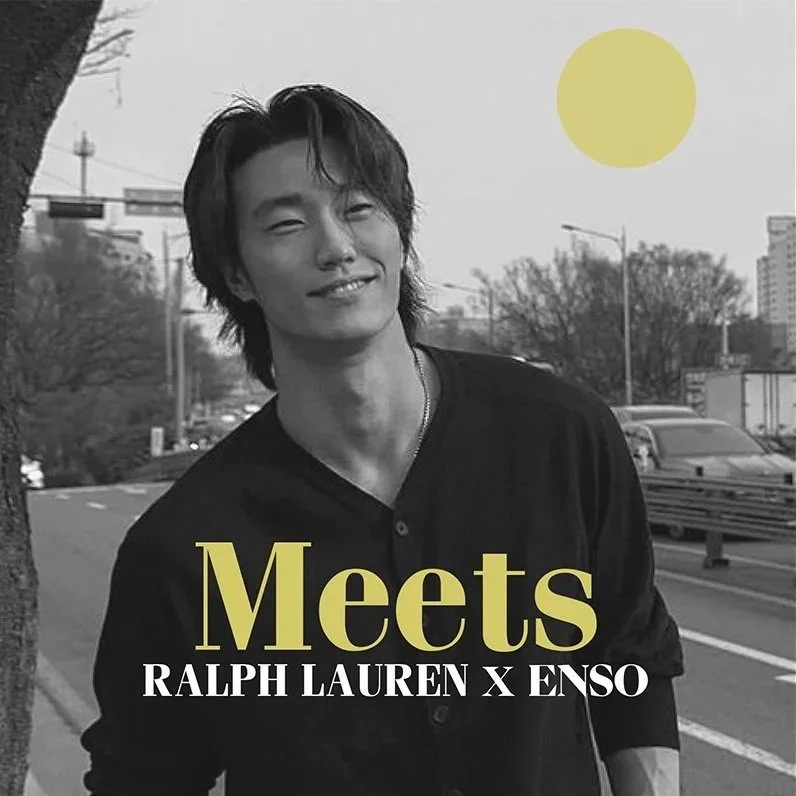 Black and white photo of a smiling young man with medium-length hair, standing outdoors beside a tree, with a cityscape and cars in the background, a yellow sun in the sky, and yellow and white text overlay, reading 'Meets Ralph Lauren x Enso.'
