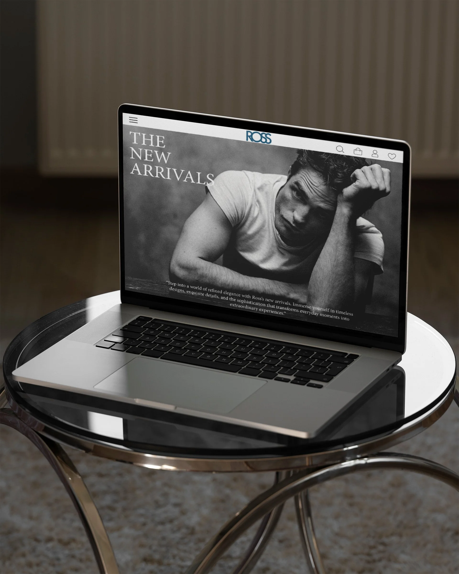 A laptop displaying a black and white fashion website on a glass-topped table with a modern curved metal base.