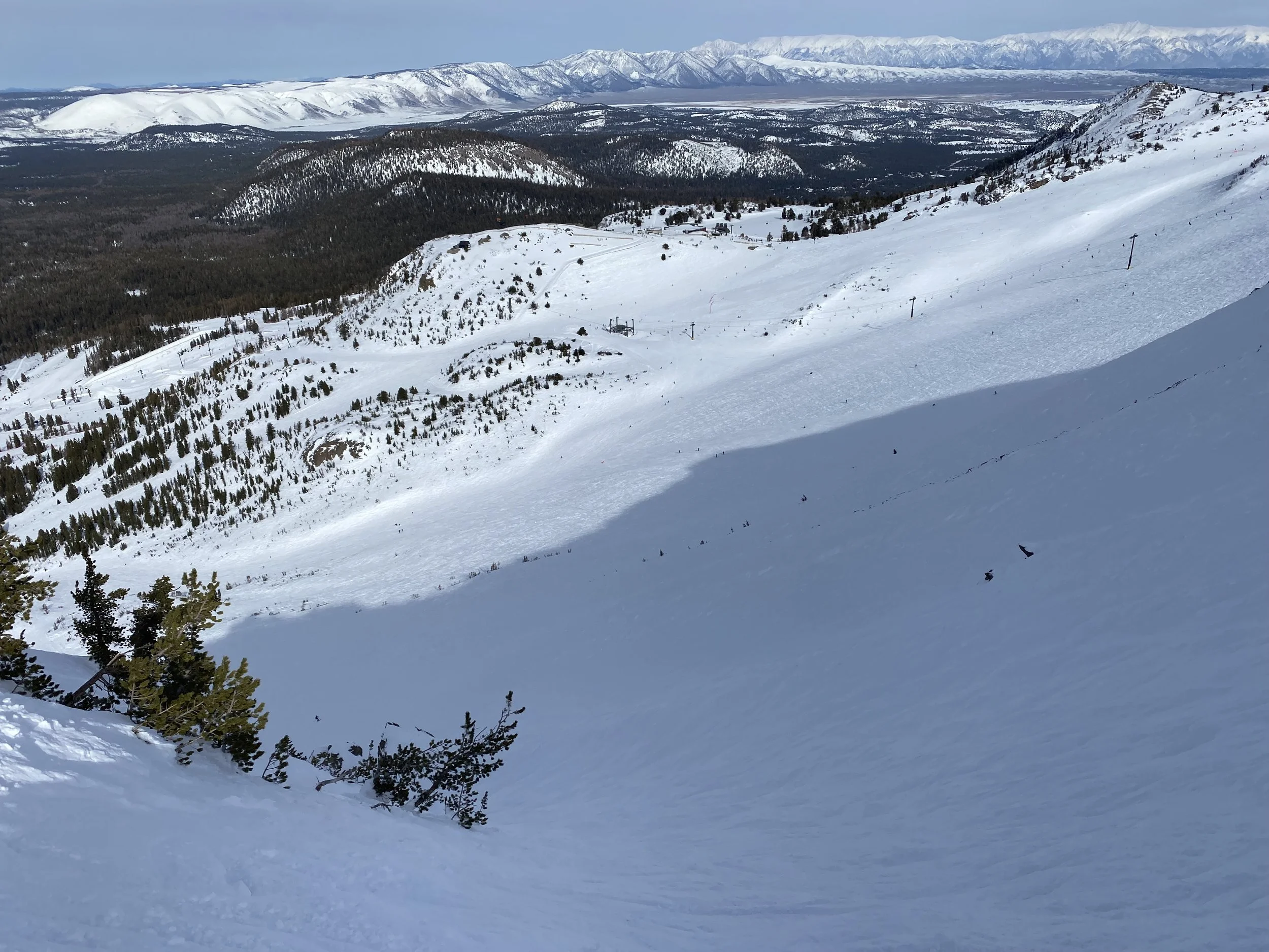 Snow-covered mountain landscape with ski slopes, ski lift poles, and distant mountain range in the background.