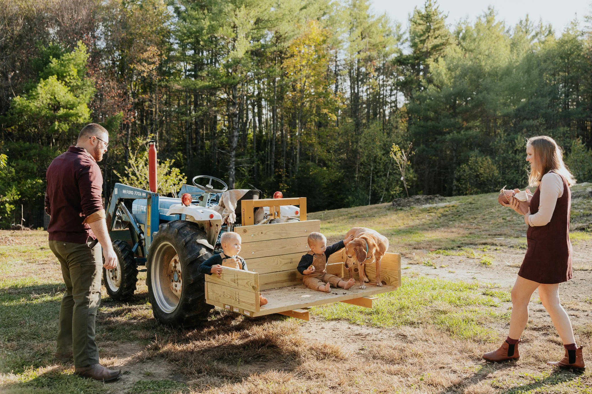 Family with young children and dog on a tractor trailer outdoors in a rural area with trees