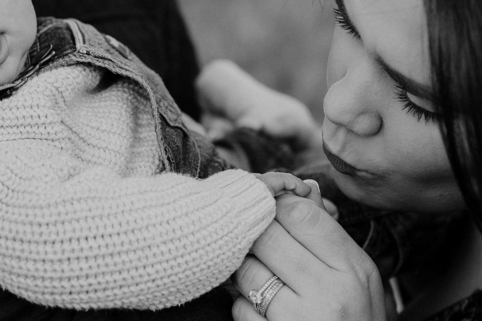 A woman gently holding a child's hand close to her face, showing intimacy and tenderness in a black and white photo.