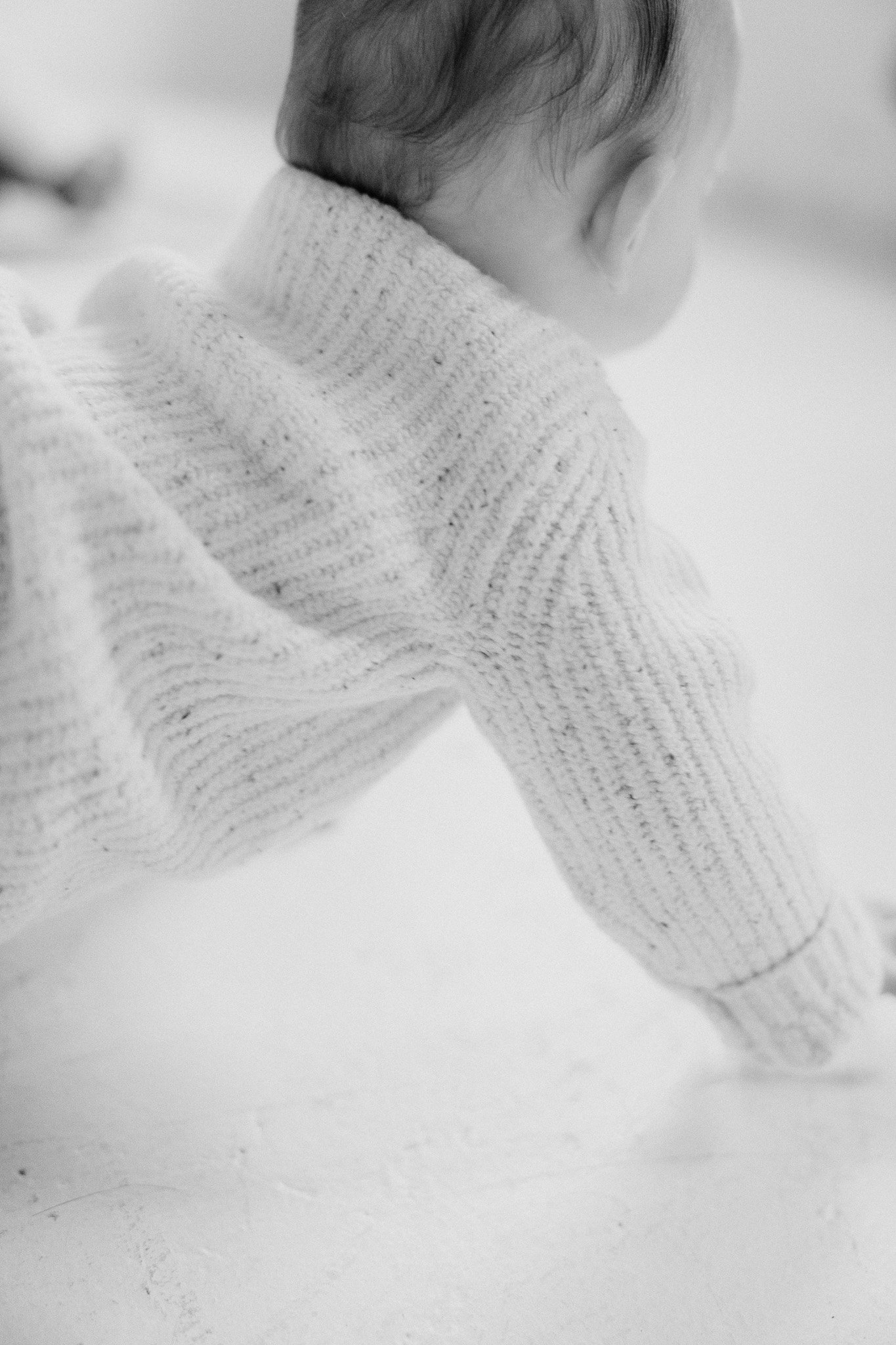 Close-up of a baby crawling on a smooth surface, wearing a cozy knit sweater.