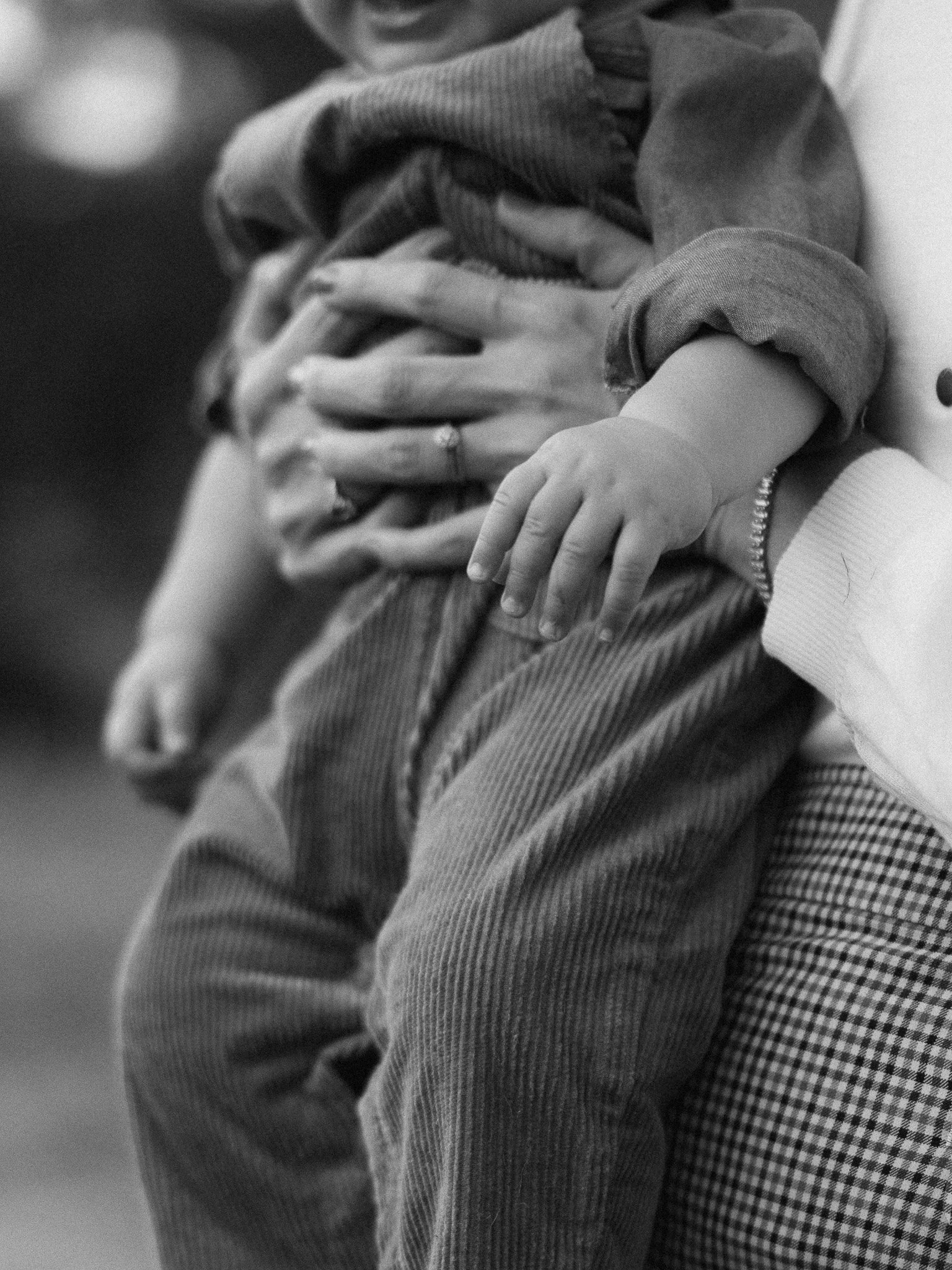 Close-up of a child's arm and hand resting on an adult's arm, with the adult's hand gently holding the child's side. The image is in black and white.