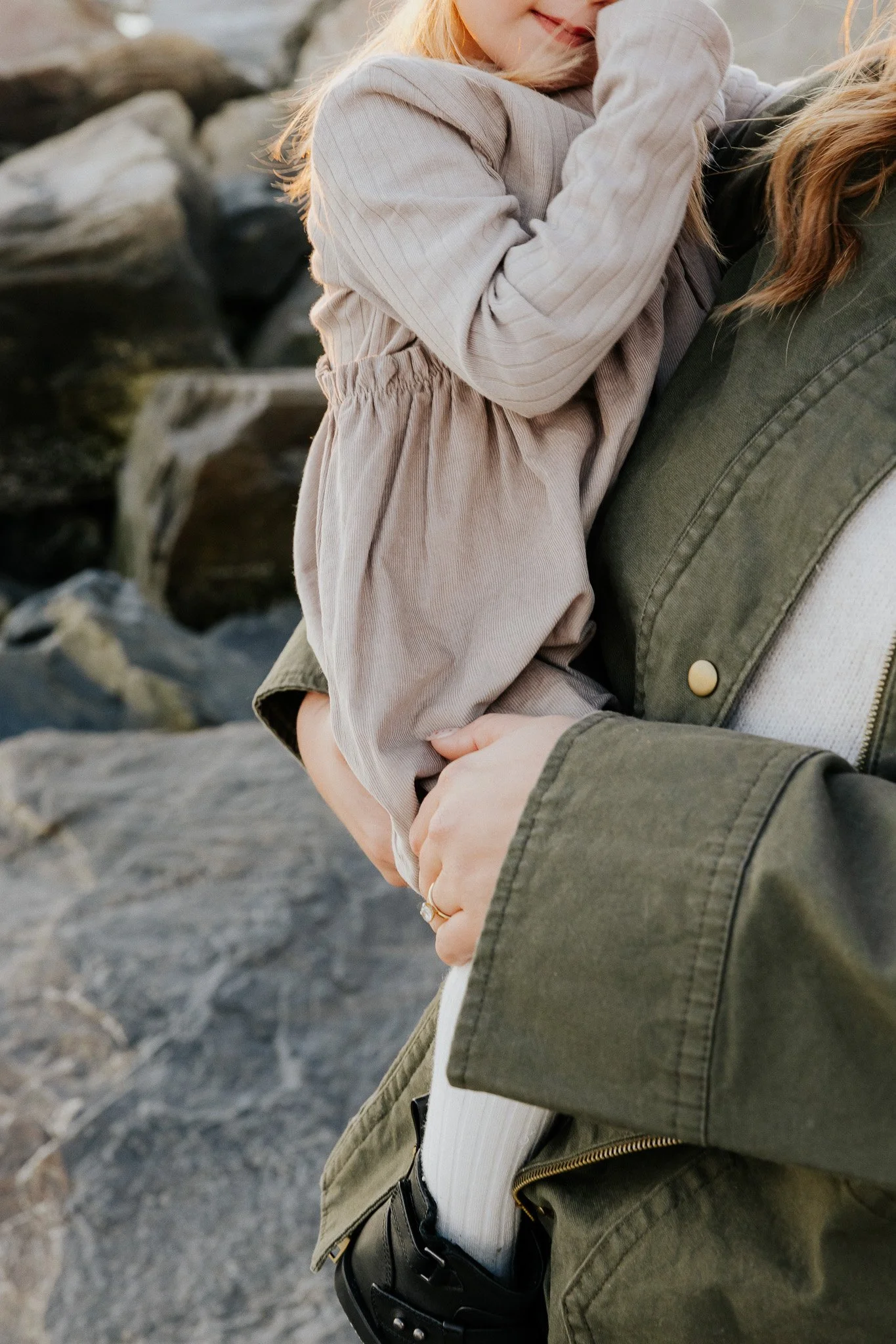 A person holding a young girl in their arms outdoors near rocks.