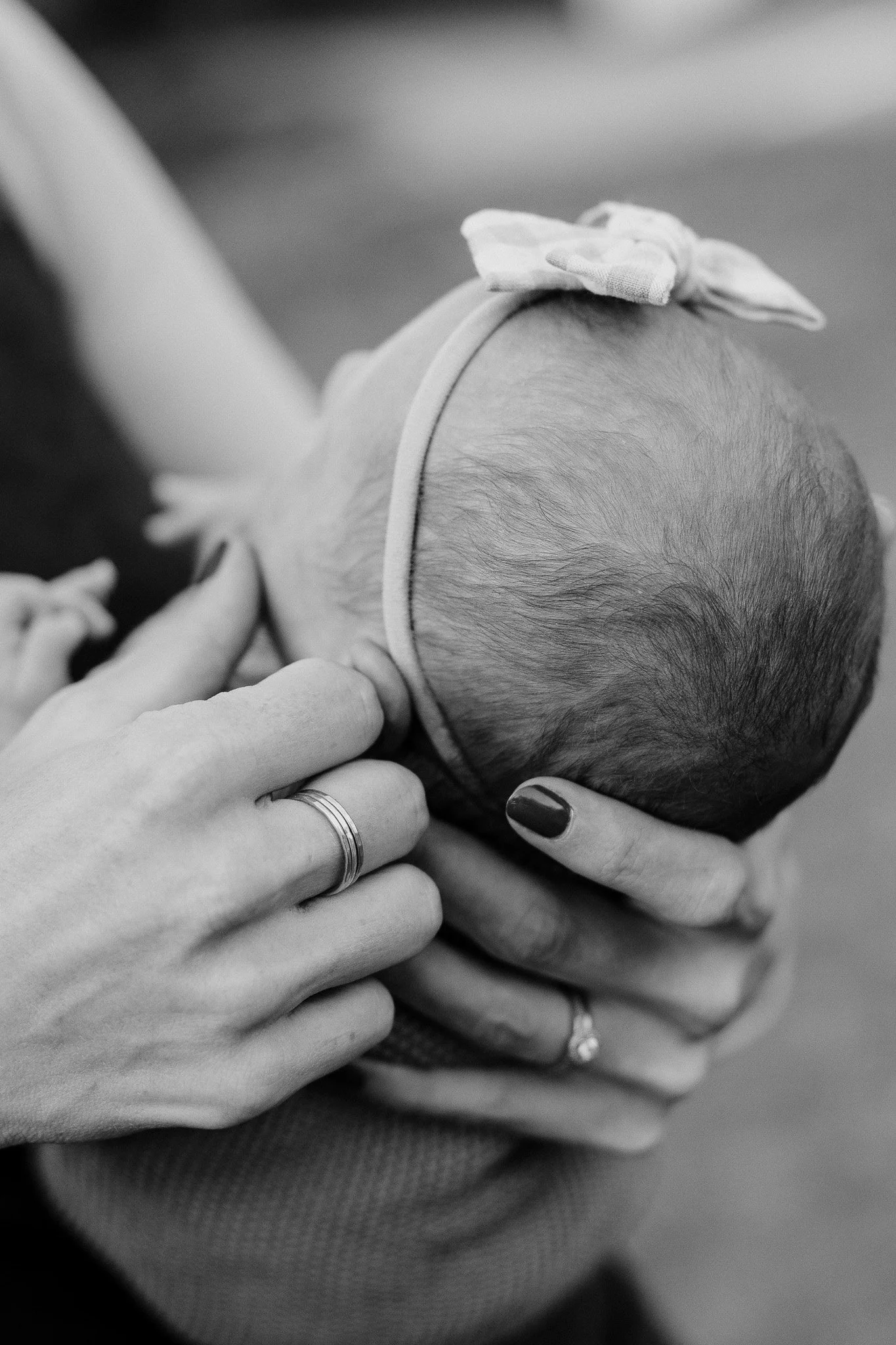 Black and white photo of a baby being held gently by two adults, focusing on the baby's head and the adult's hands.