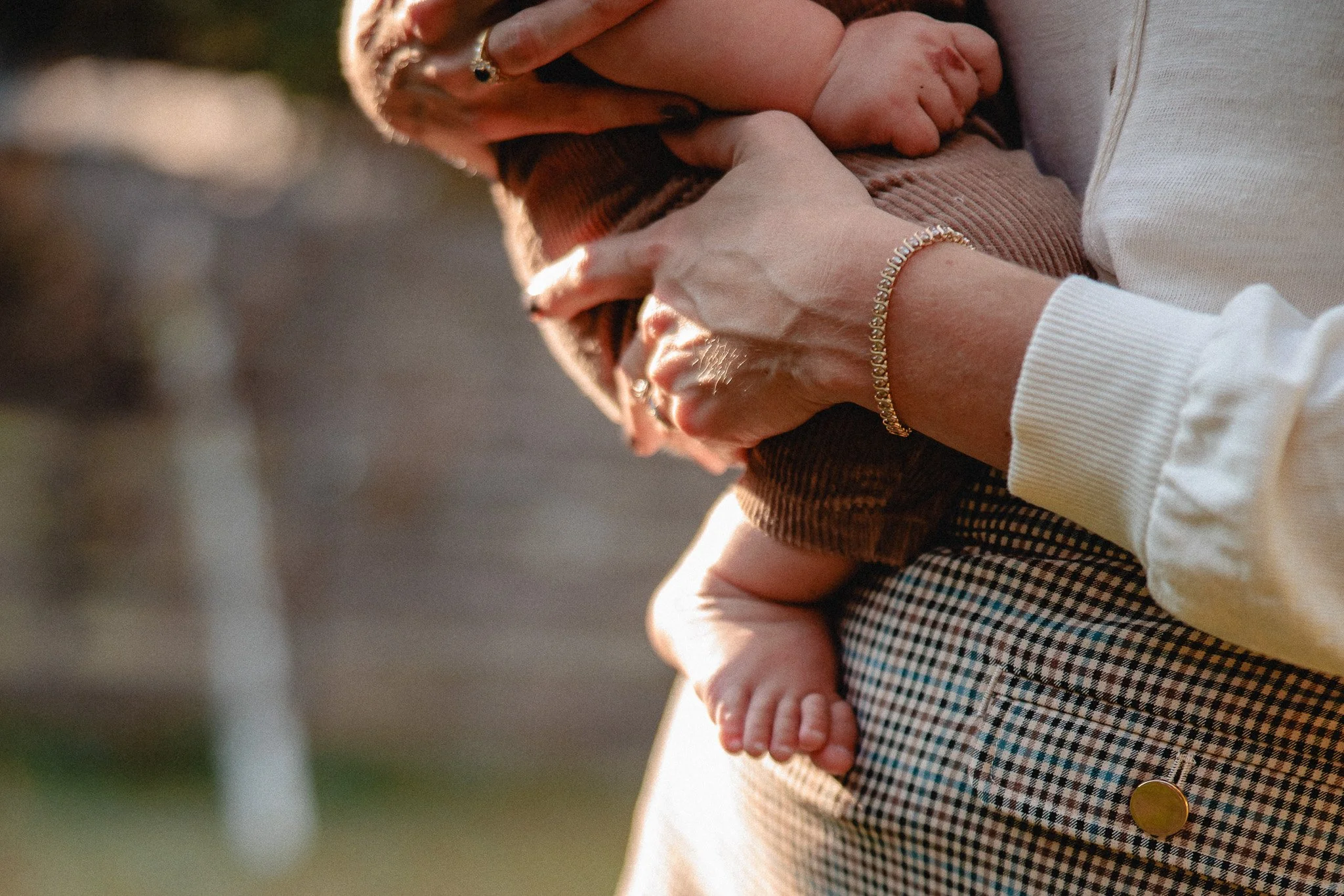 An adult holding a baby, showing close-up of their hands and baby's feet in an outdoor setting.