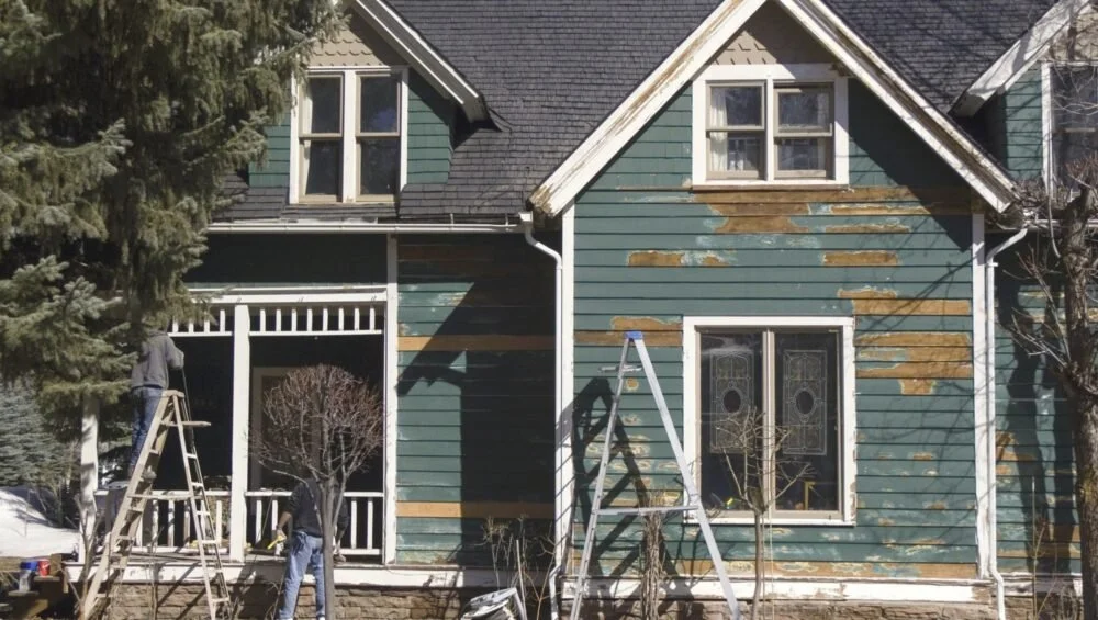 Worker on a ladder renovating the exterior of an older two-story house