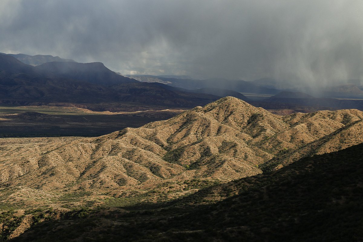 Deeply eroded granite hills in Tonto Basin illuminated between dark shadows and storm clouds.