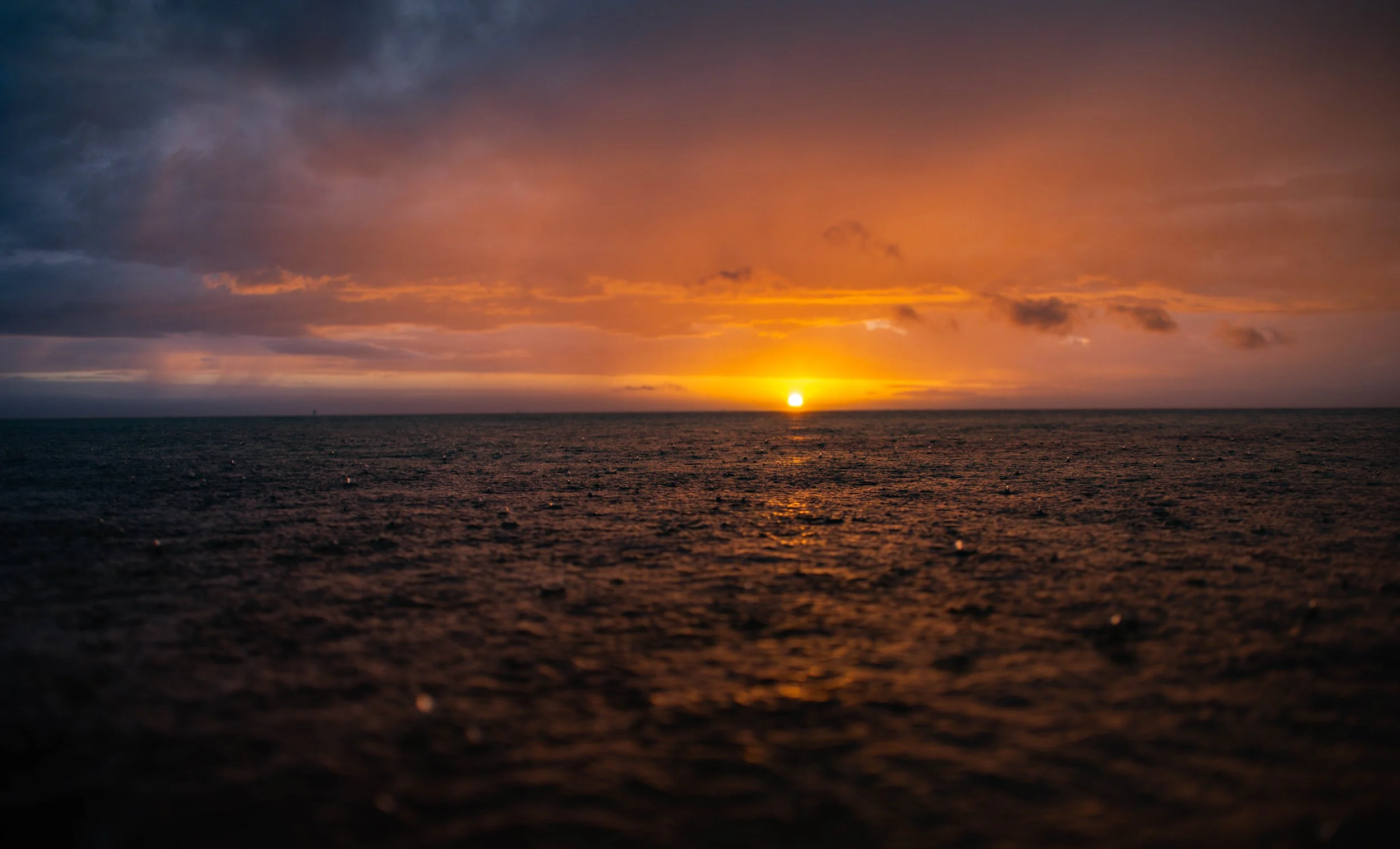 A sunset over the ocean with colorful clouds in the sky, casting a warm glow on the water