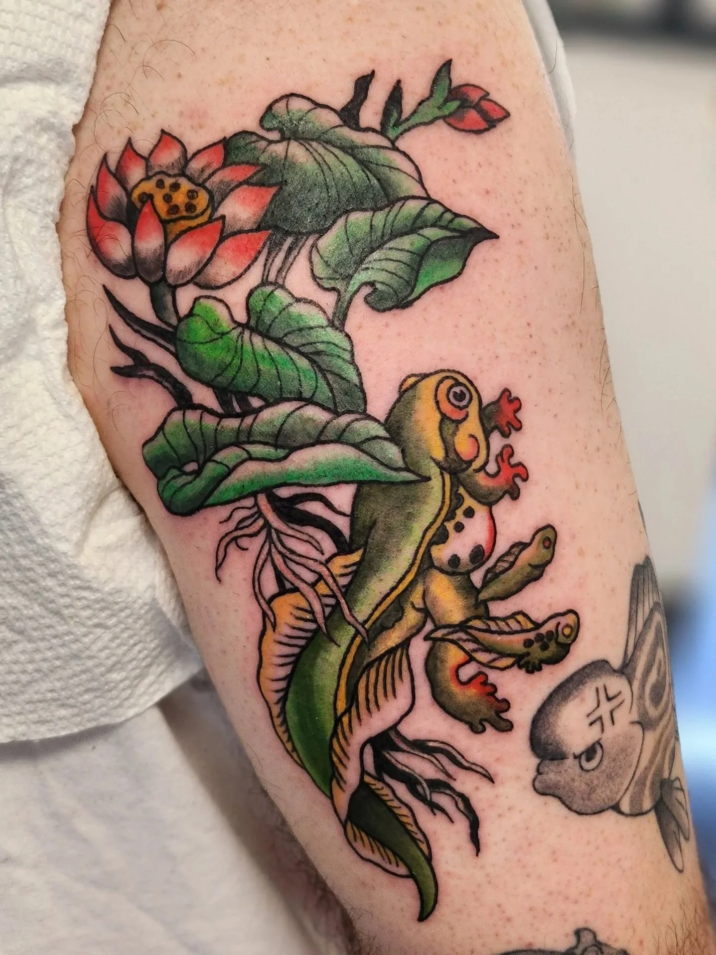 Colorful tattoo of a frog climbing a leafy plant with a flower at the top and a small creature at the bottom.