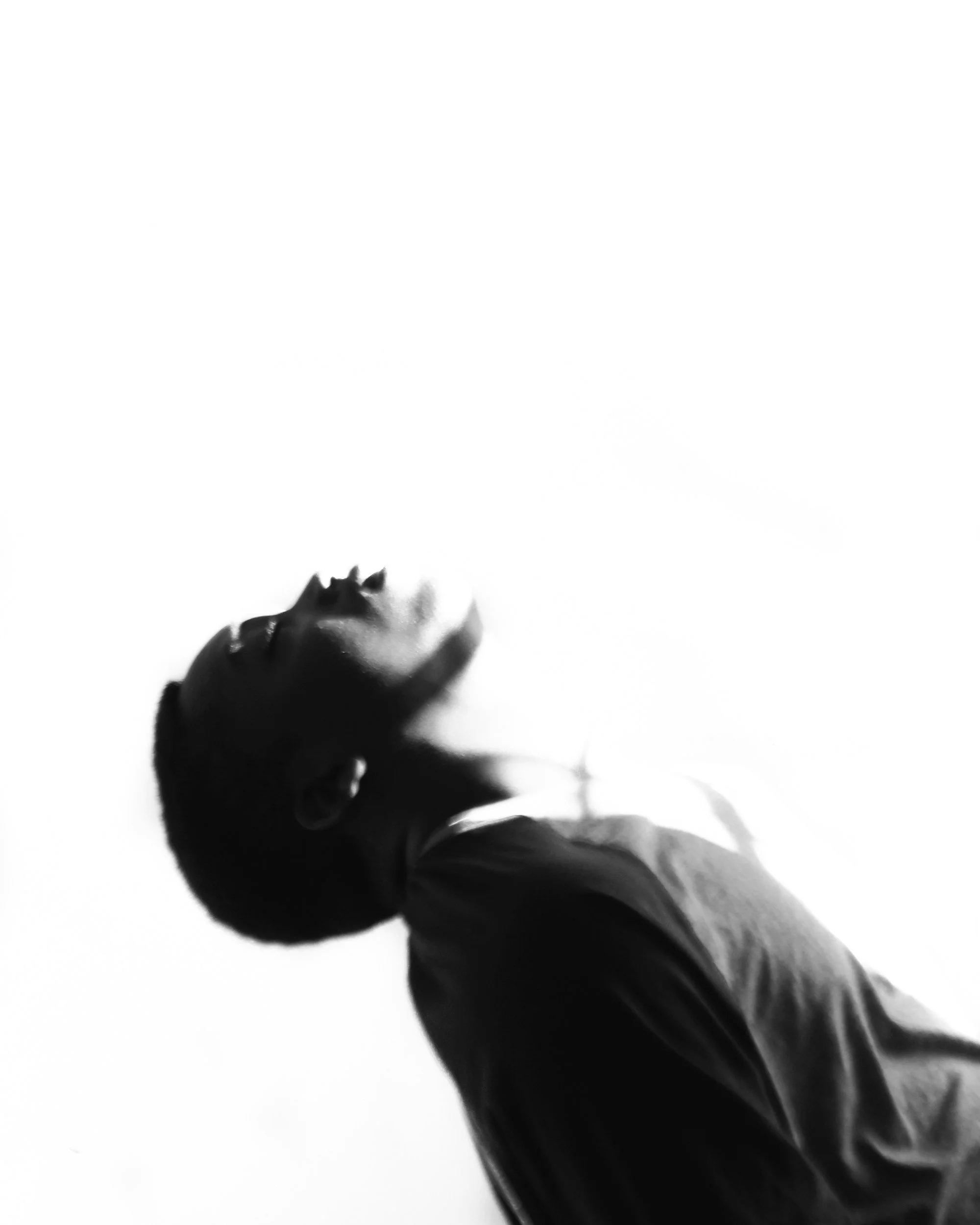 Black and white photo of a person with closed eyes, head tilted back, and facing upward, with high contrast lighting.