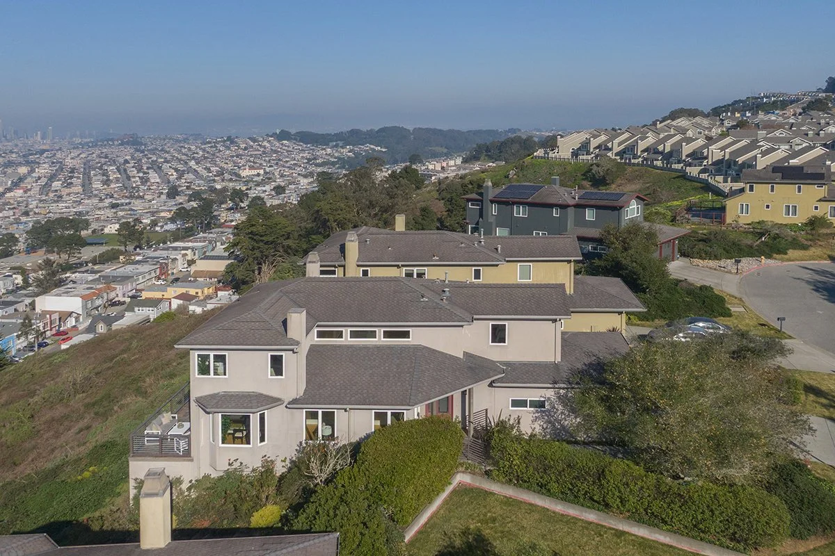 Houses on a hillside overlooking a cityscape in San Francisco, California, with trees and clear blue sky.