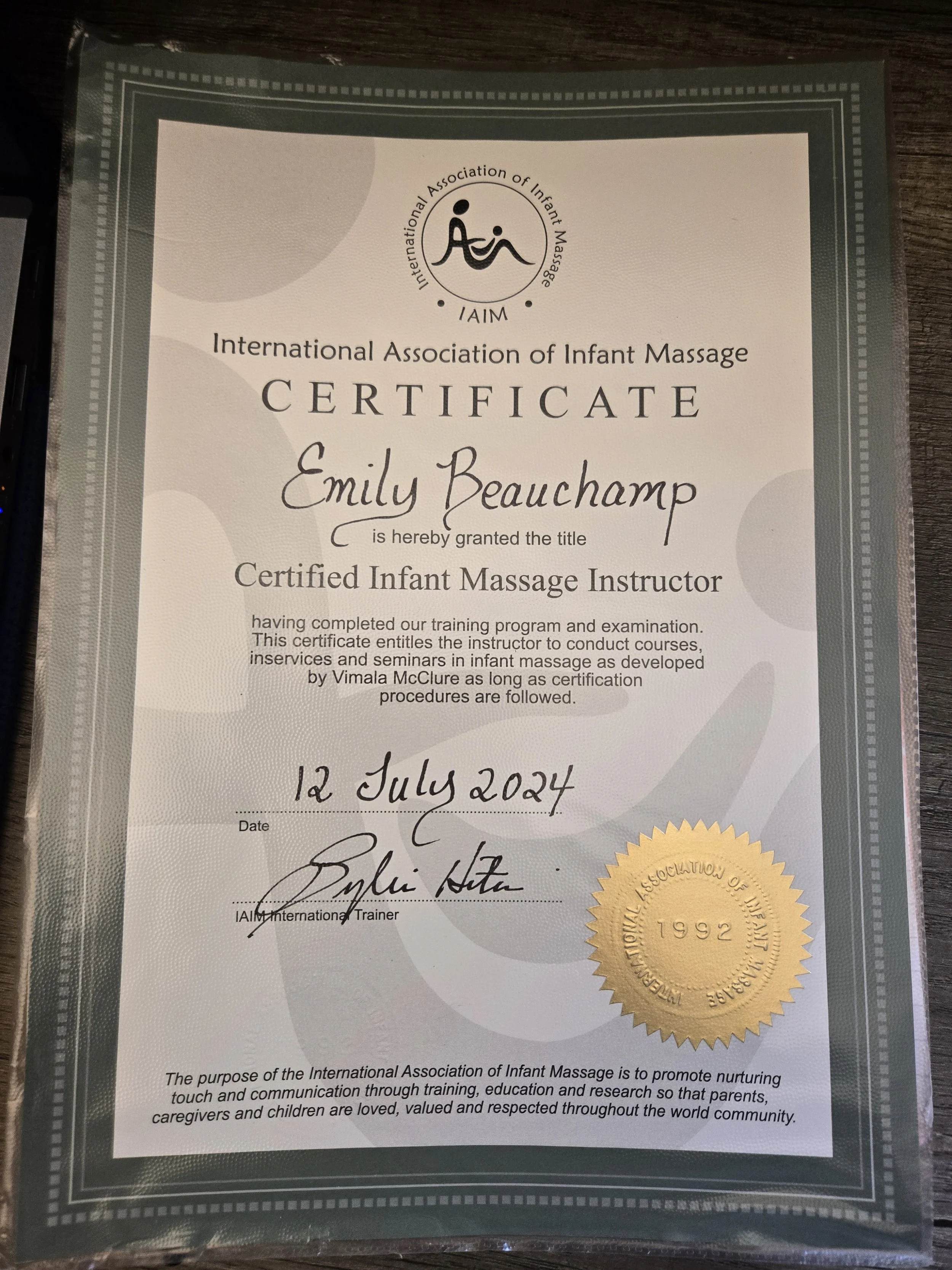 Certificate from the International Association of Infant Massage awarded to Emily Beauchamp on July 12, 2024, with a gold seal and signature.