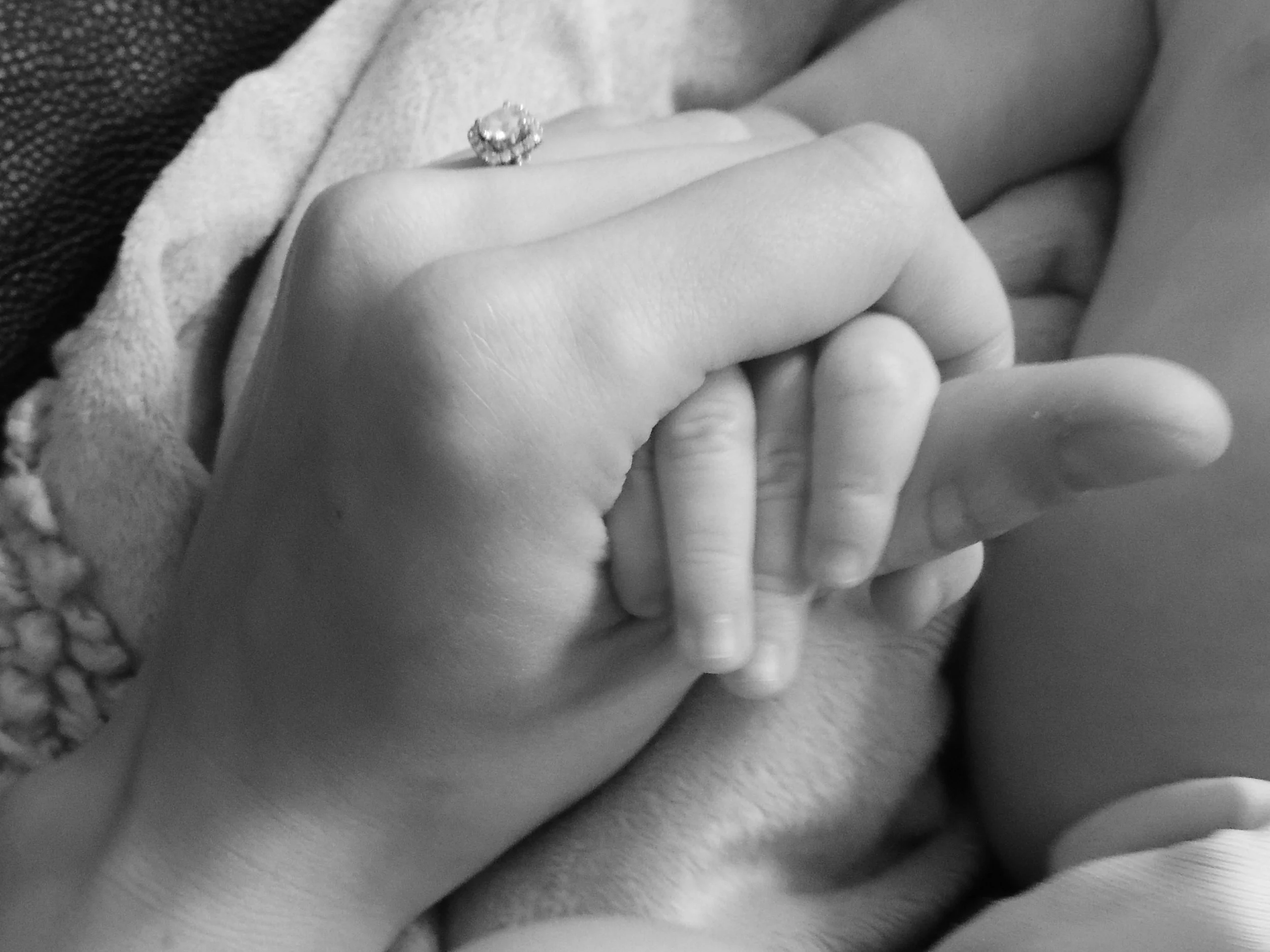 Close-up of two hands clasped, one with an engagement ring with a large gemstone, the other an infant's hand.