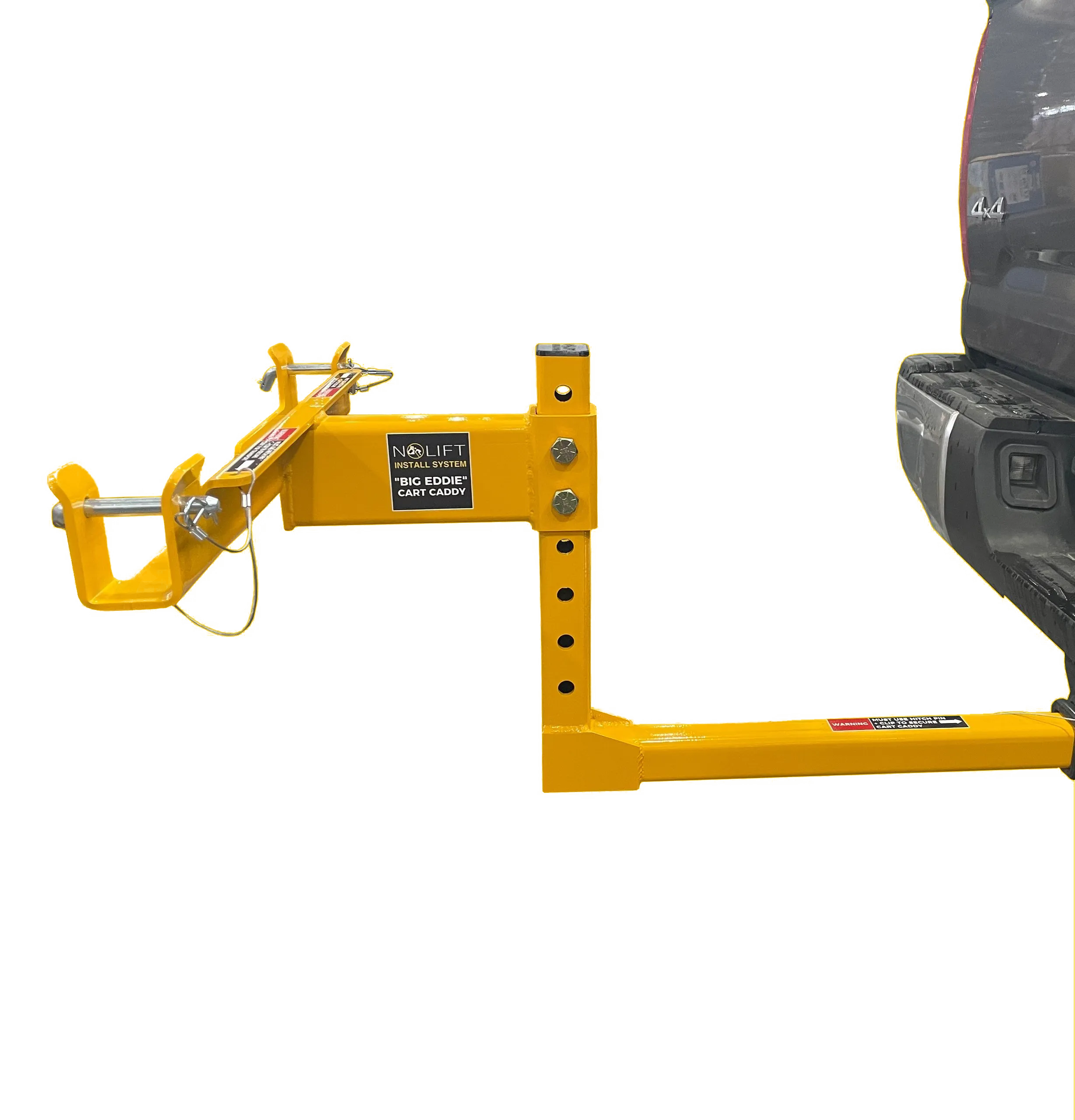 A black pickup truck is parked next to a bright yellow cart caddy labeled Big Eddie. The cart caddy is designed for installing lift systems. Part of the truck's rear and tire are visible on the right side of the image.
