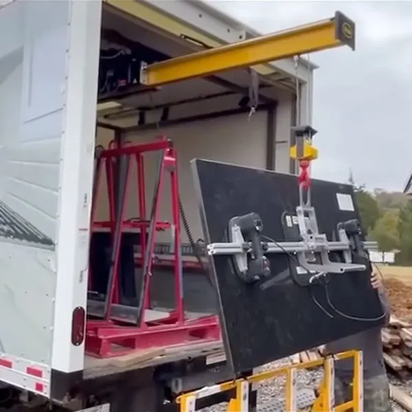 A large flat-screen TV is being lifted out of a moving truck using a motorized hoist system with a red strap and yellow support beam.