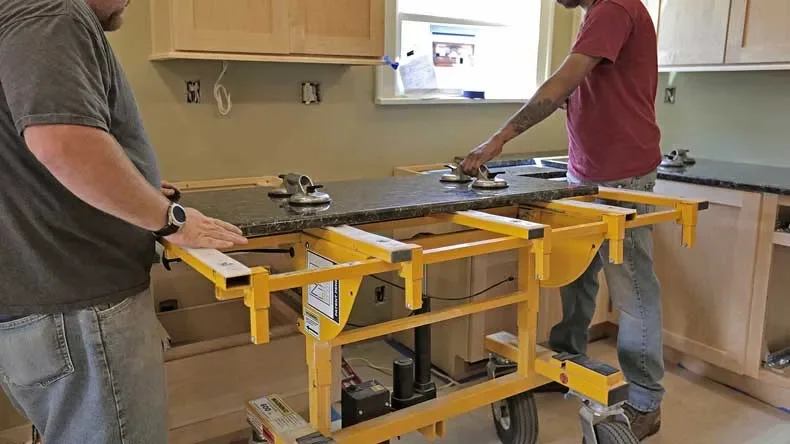Two men installing a granite countertop in a kitchen, using a portable siding and measuring tool.